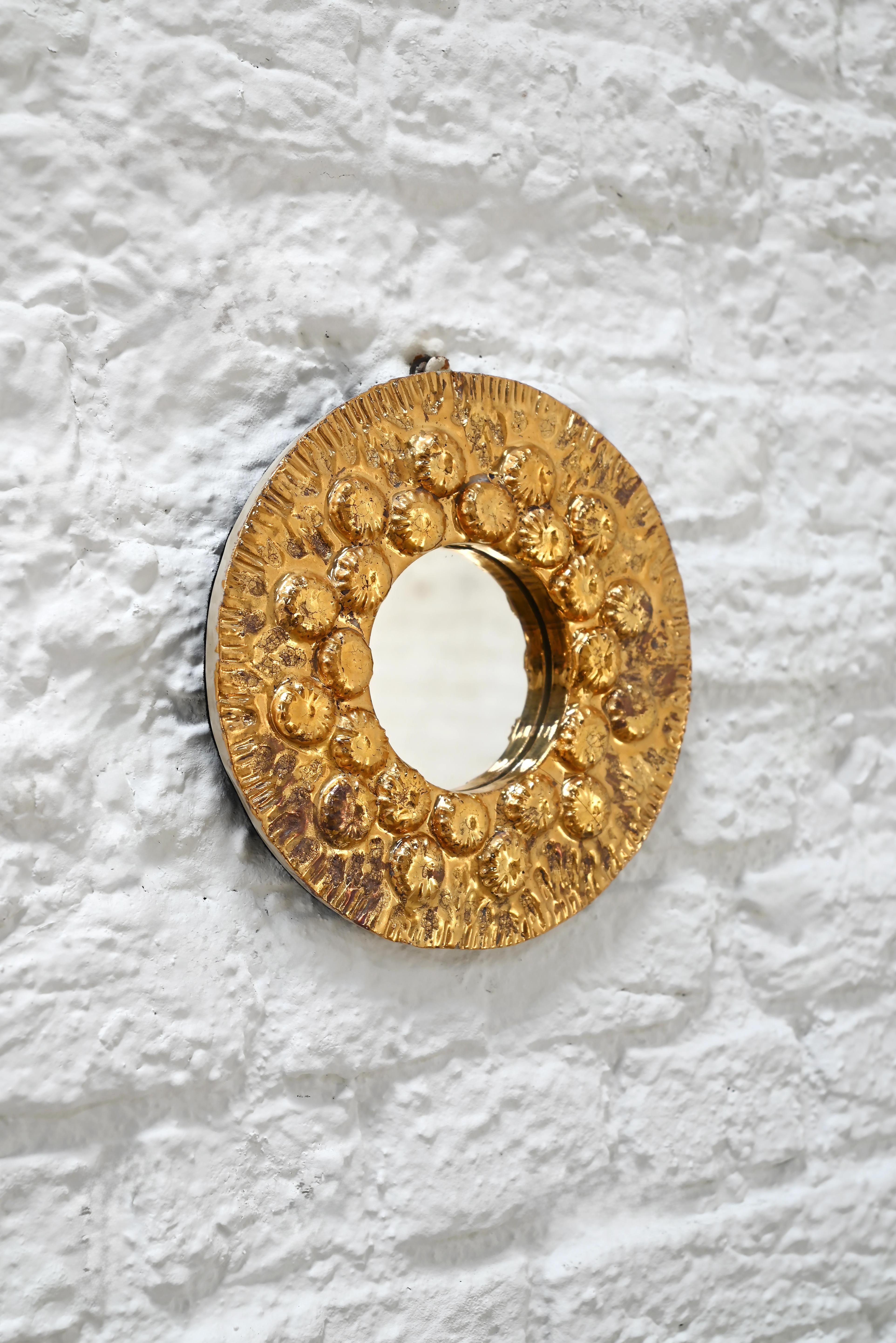 Ce miroir rond en céramique est synonyme de chaleur et de brillance. Fini dans une riche glaçure dorée avec un motif texturé, presque en forme de soleil, de détails circulaires en relief, il capte magnifiquement la lumière sous tous les angles. Le