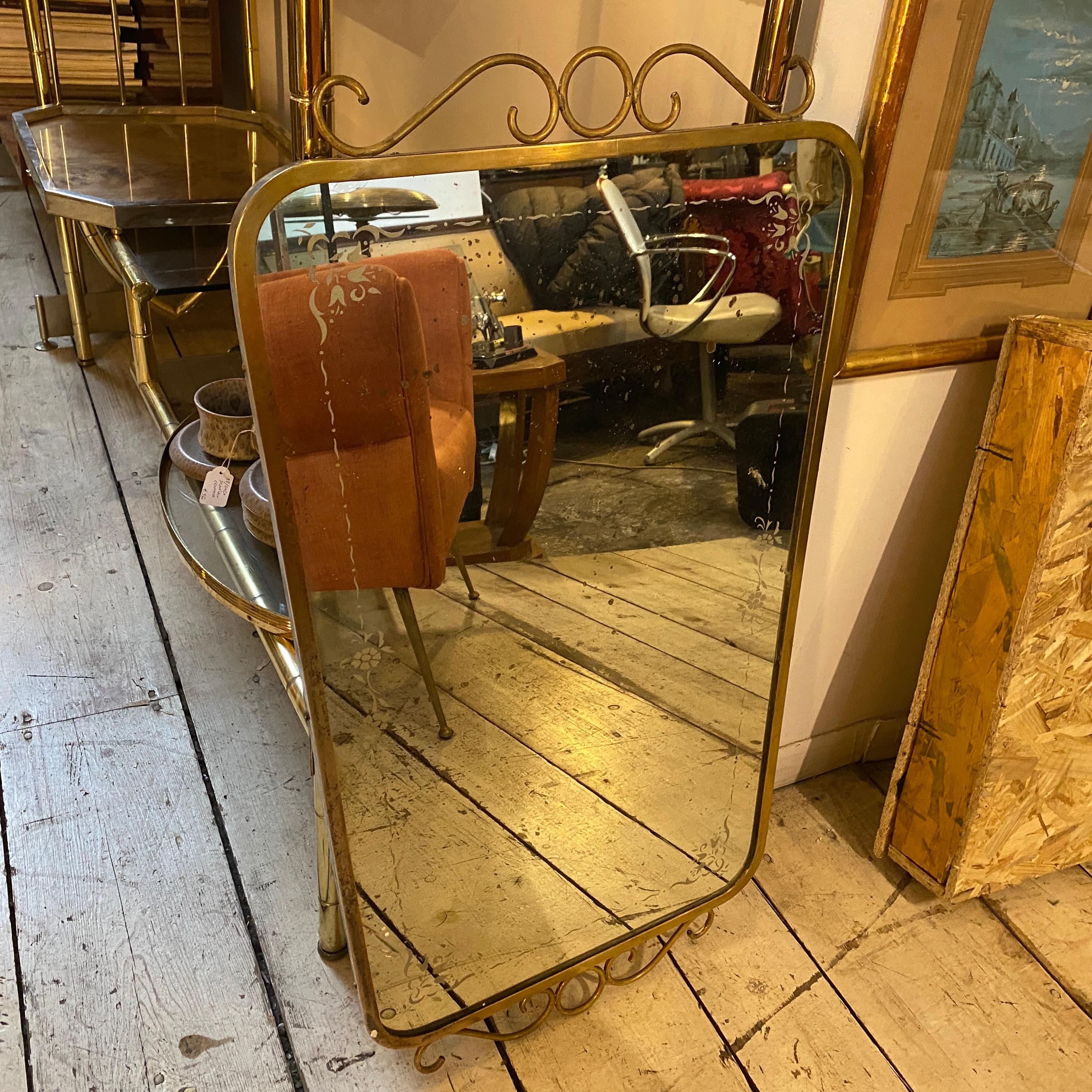 A Mid-Century Modern solid brass and etched glass wall mirror designed and manufactured in Italy in the Fifties in the manner of Gio Ponti. The brass it's in original patina, the original etched glass it's decorated with floral motifs and it has