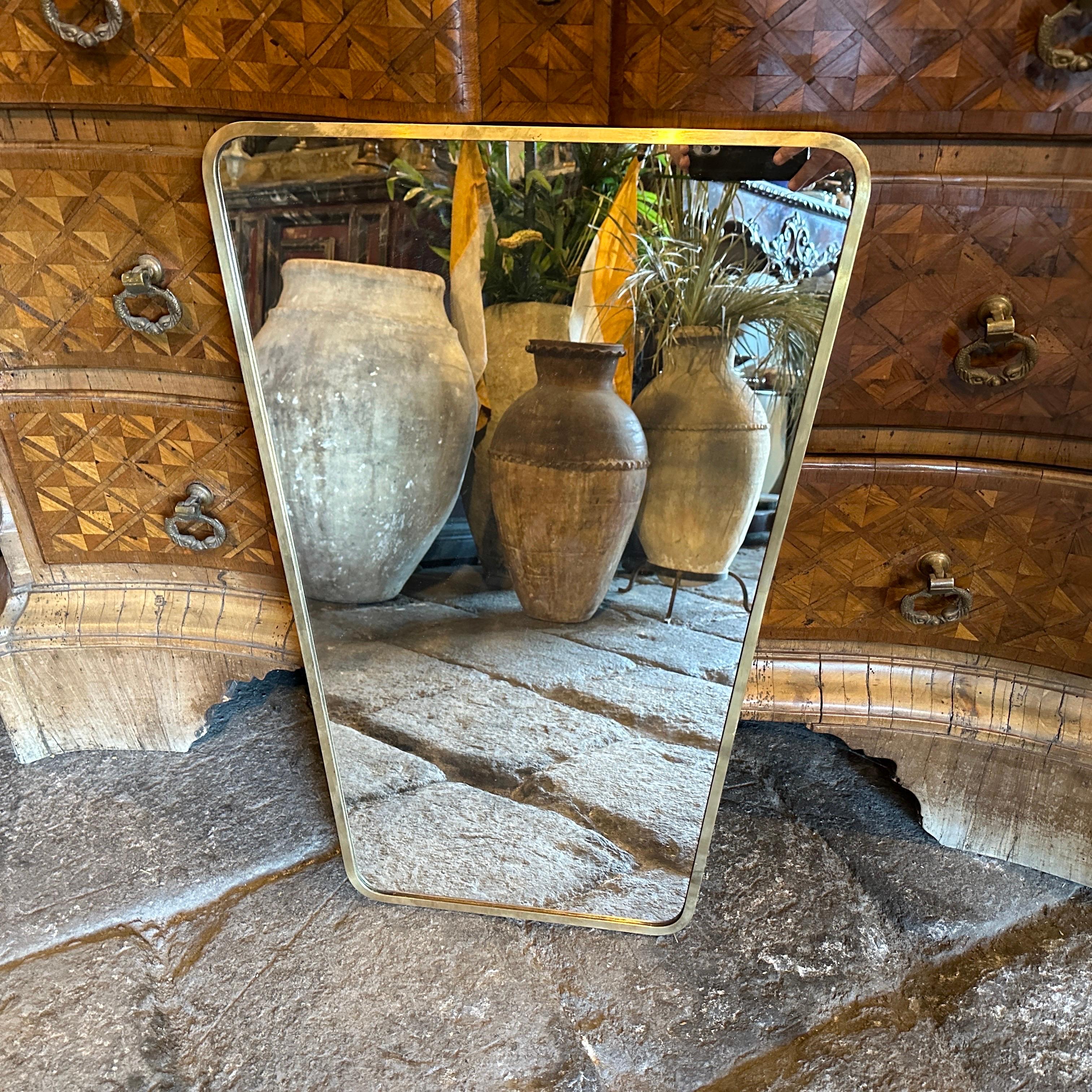 Miroir mural en laiton massif conçu et fabriqué en Italie à la manière de Gio Ponti, qui utilisait ce type de miroir dans les plus belles maisons de Milan dans les années 50. Le laiton présente une belle patine d'origine, tandis que le verre reste