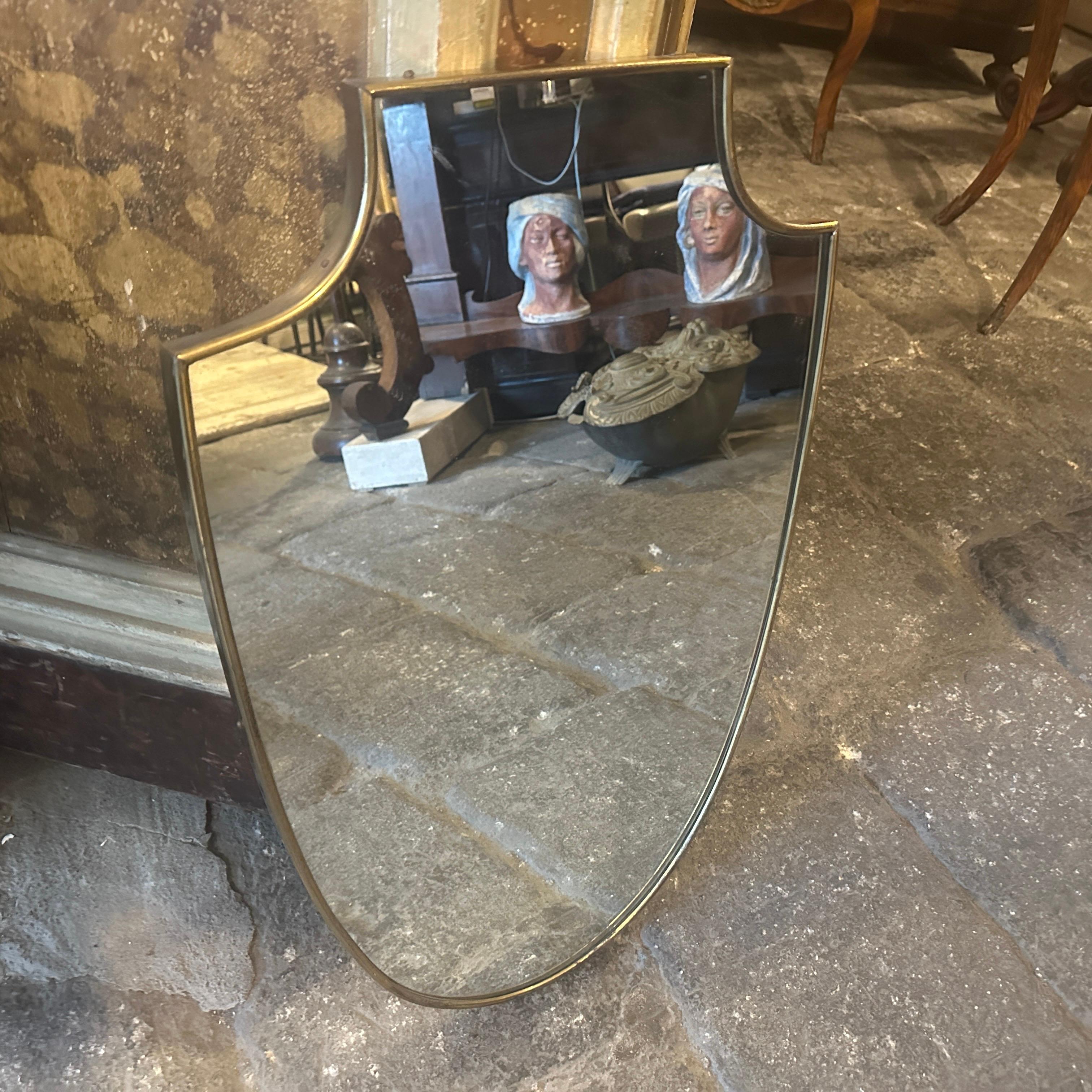 Miroir mural en laiton massif conçu et fabriqué en Italie à la manière de Gio Ponti, qui utilisait ce type de miroir dans les plus belles maisons de Milan dans les années 50. Le laiton présente une belle patine d'origine, tandis que le verre reste