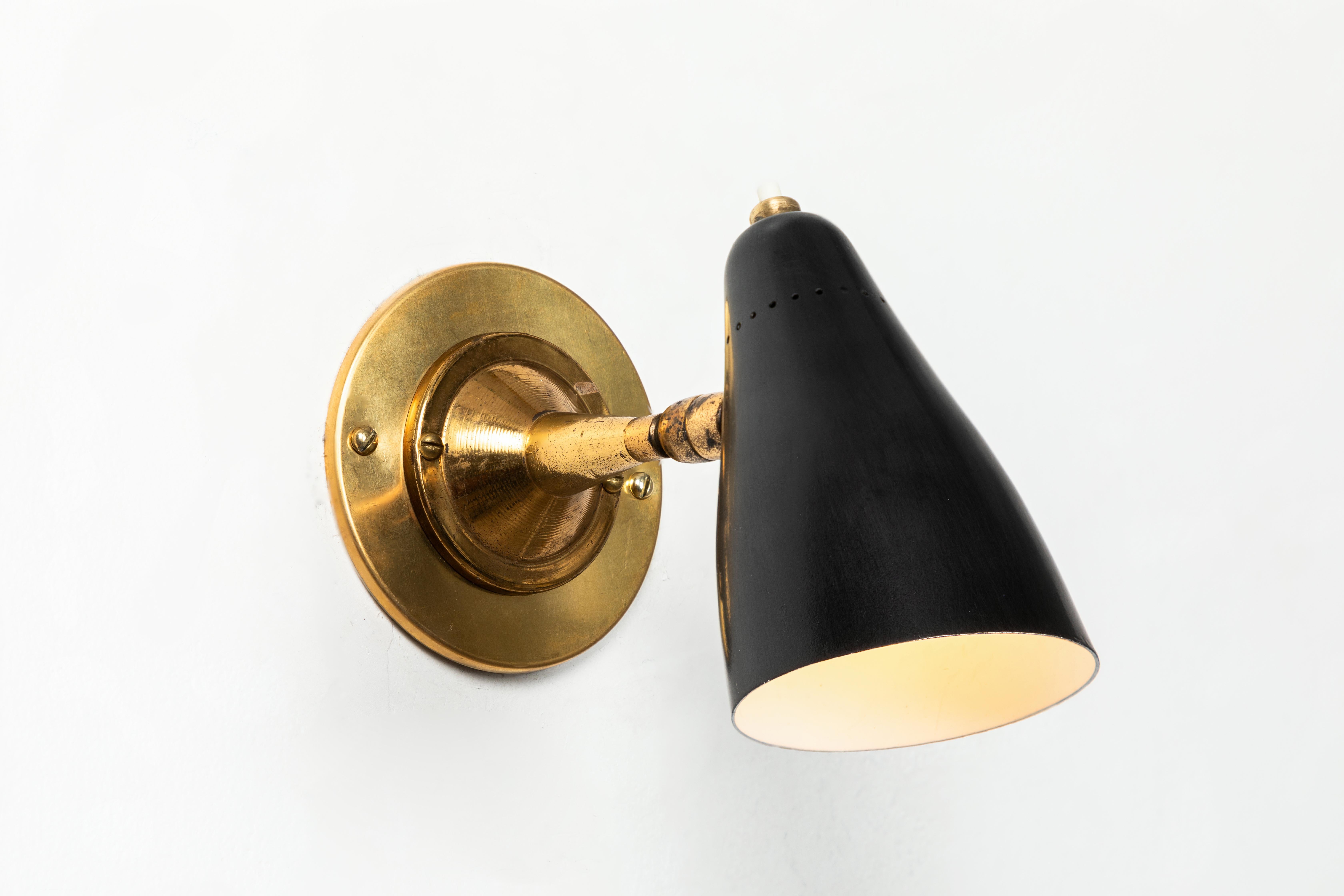 1950s Giuseppe Ostuni articulating sconces for O-Luce. Executed in brass and black painted aluminium with perforated shade. Sconces pivot up/down and left/right on two separate ball joints. Original on/off switch on top of lamp. Wired for US