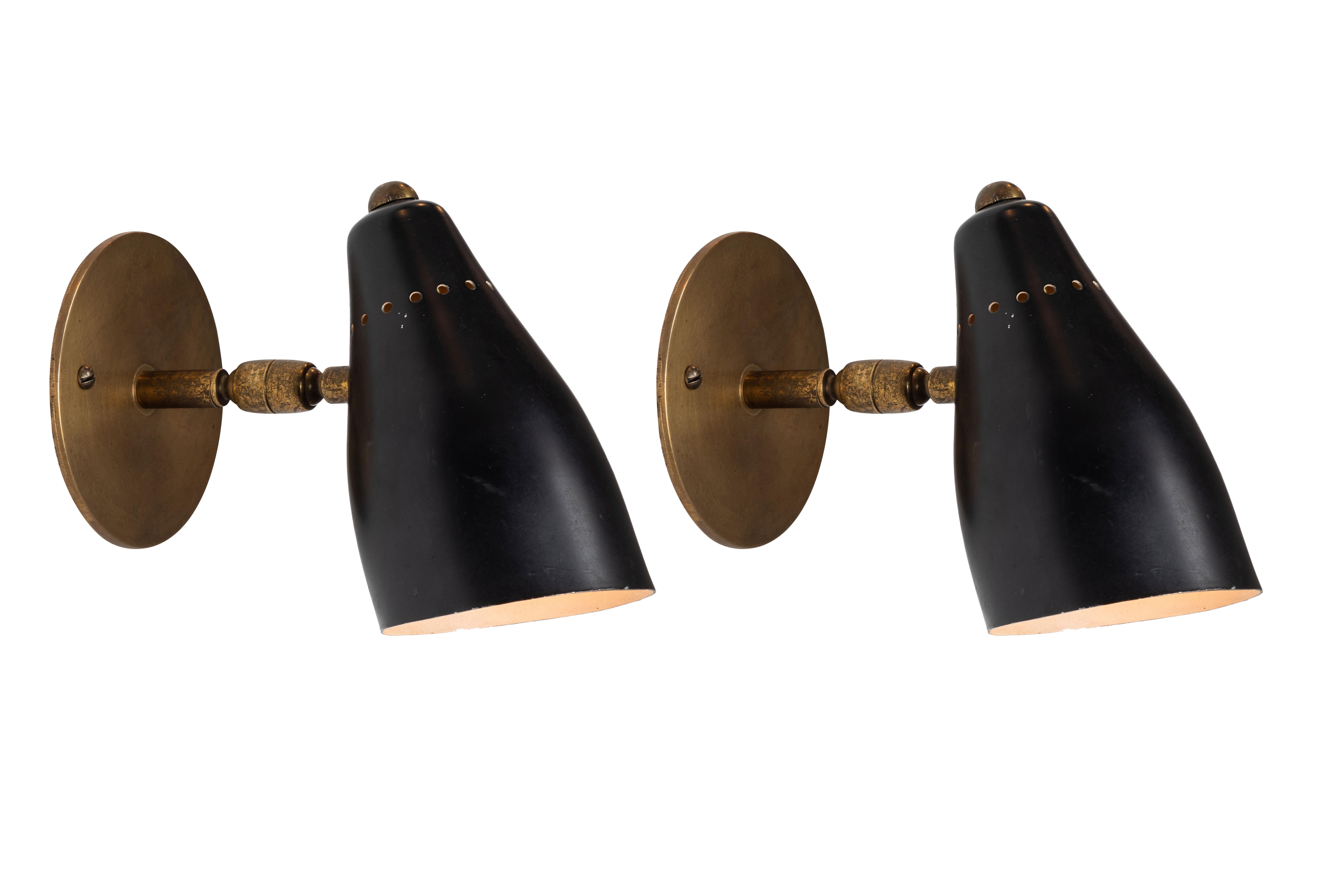 1950s Giuseppe Ostuni articulating sconces for O-Luce. Executed in brass and black painted aluminium with perforated shade. Sconces pivot up/down and left/right on two separate ball joints. Original on/off switch on top of lamp. Wired for US