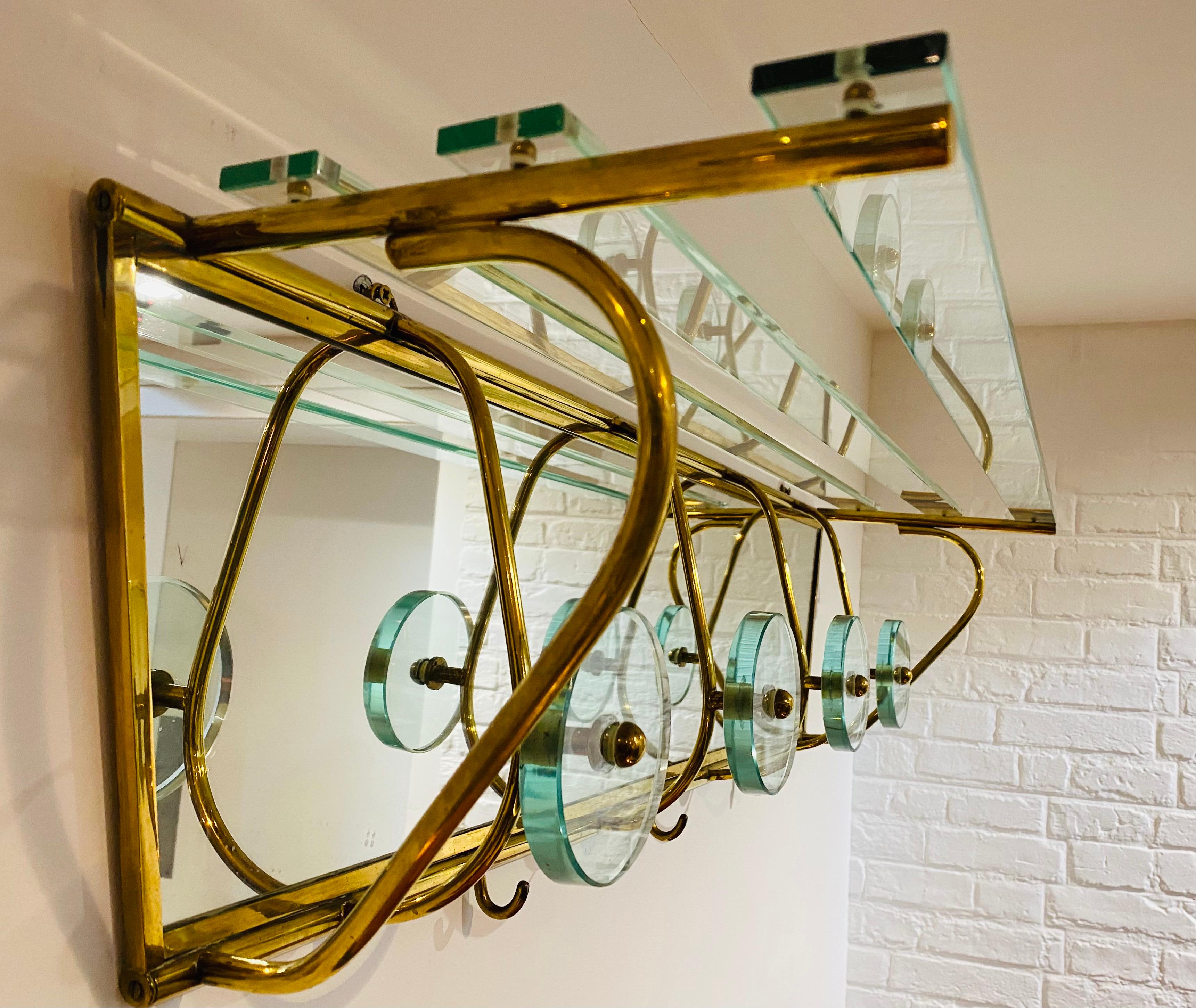 An attractive glass and brass Italian wall mount coat and hat rack att. to Fontana Arte. The rack consists of 4 thick glass discs on a mirrored background, 3 brass hooks, and glass shelves for hats on top.