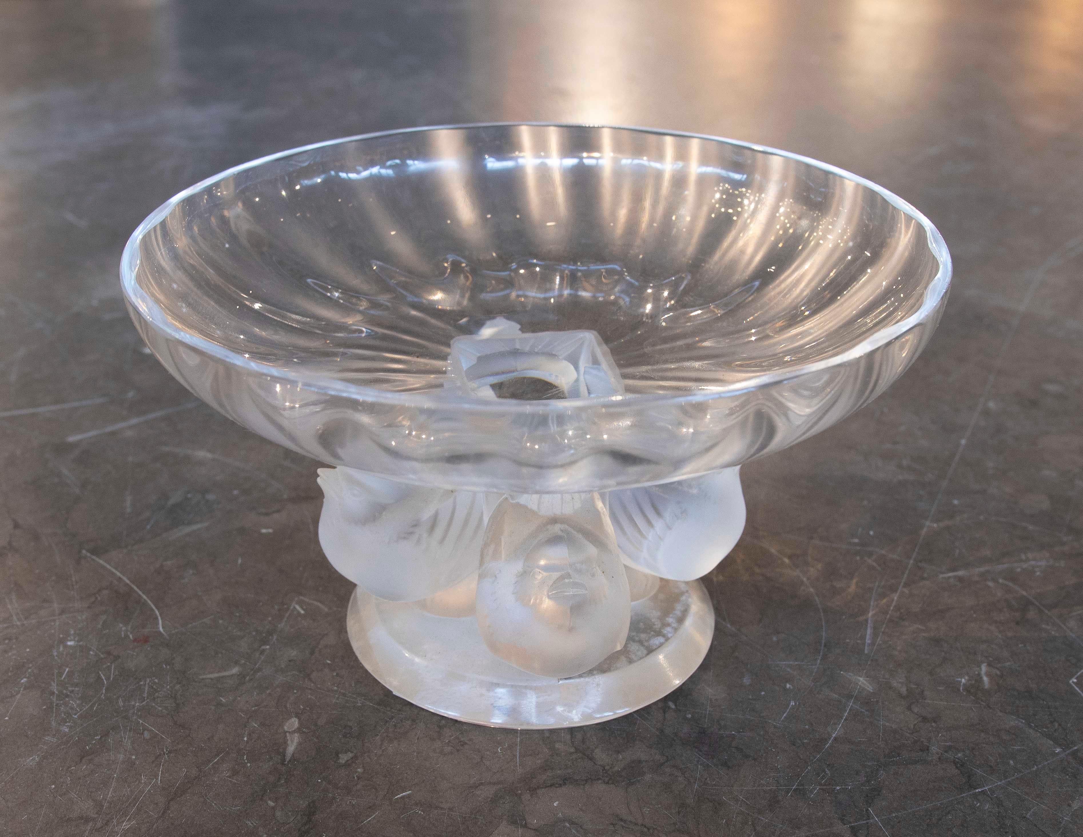 Centre de table élégant en verre transparent avec des détails givrés sur la base qui représentent des oiseaux stylisés. Son design allie fonctionnalité et esthétique, parfait pour décorer les tables ou les vitrines avec une touche de sophistication