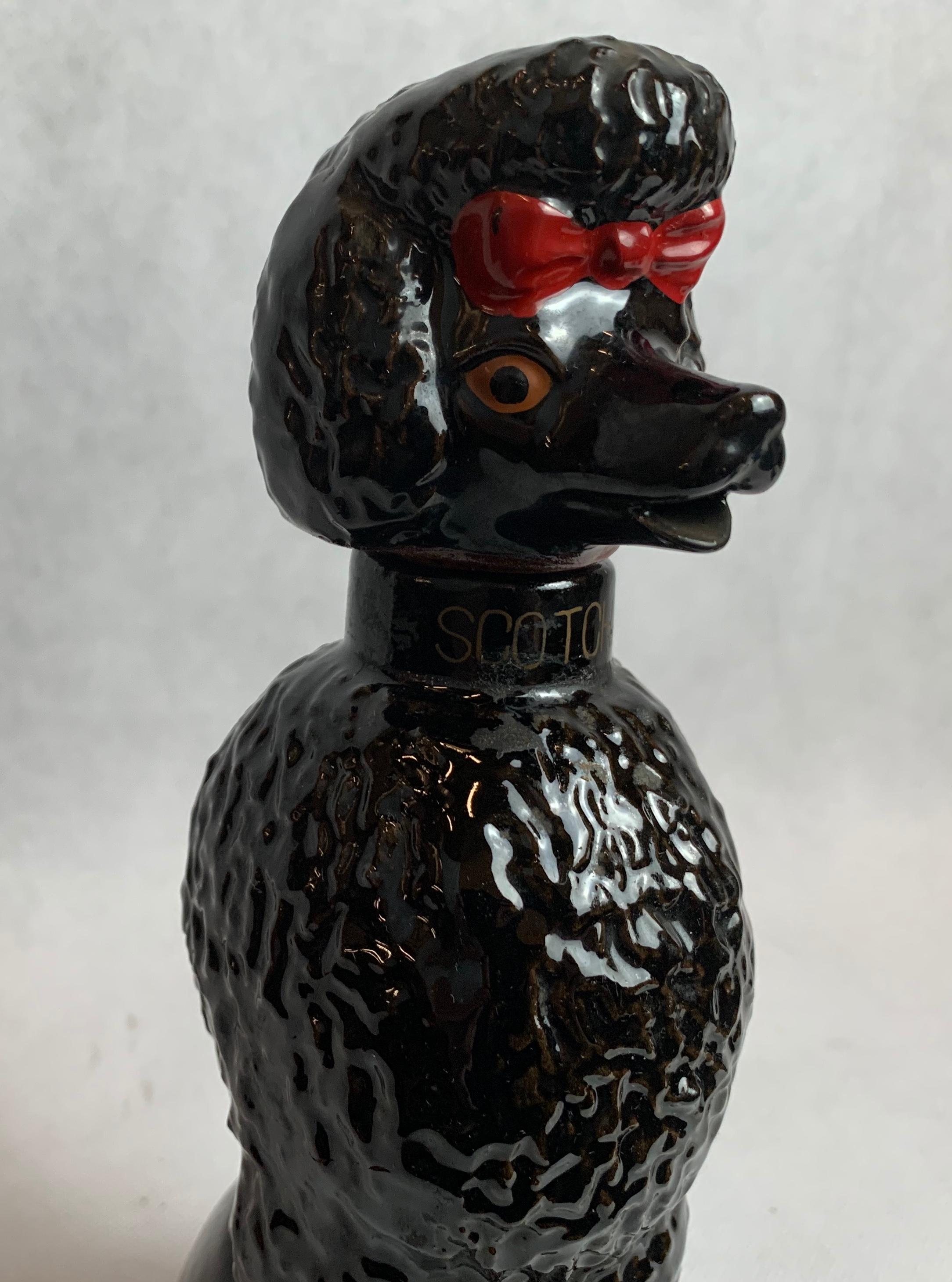 Glazed ceramic decanter marked Scotch in the form of an iconic 1950s Poodle with a smart Parisienne haircut set off with a bright red bow. When pouring Scotch it can be dispensed from the Poodles mouth. The collar is marked Scotch in gold