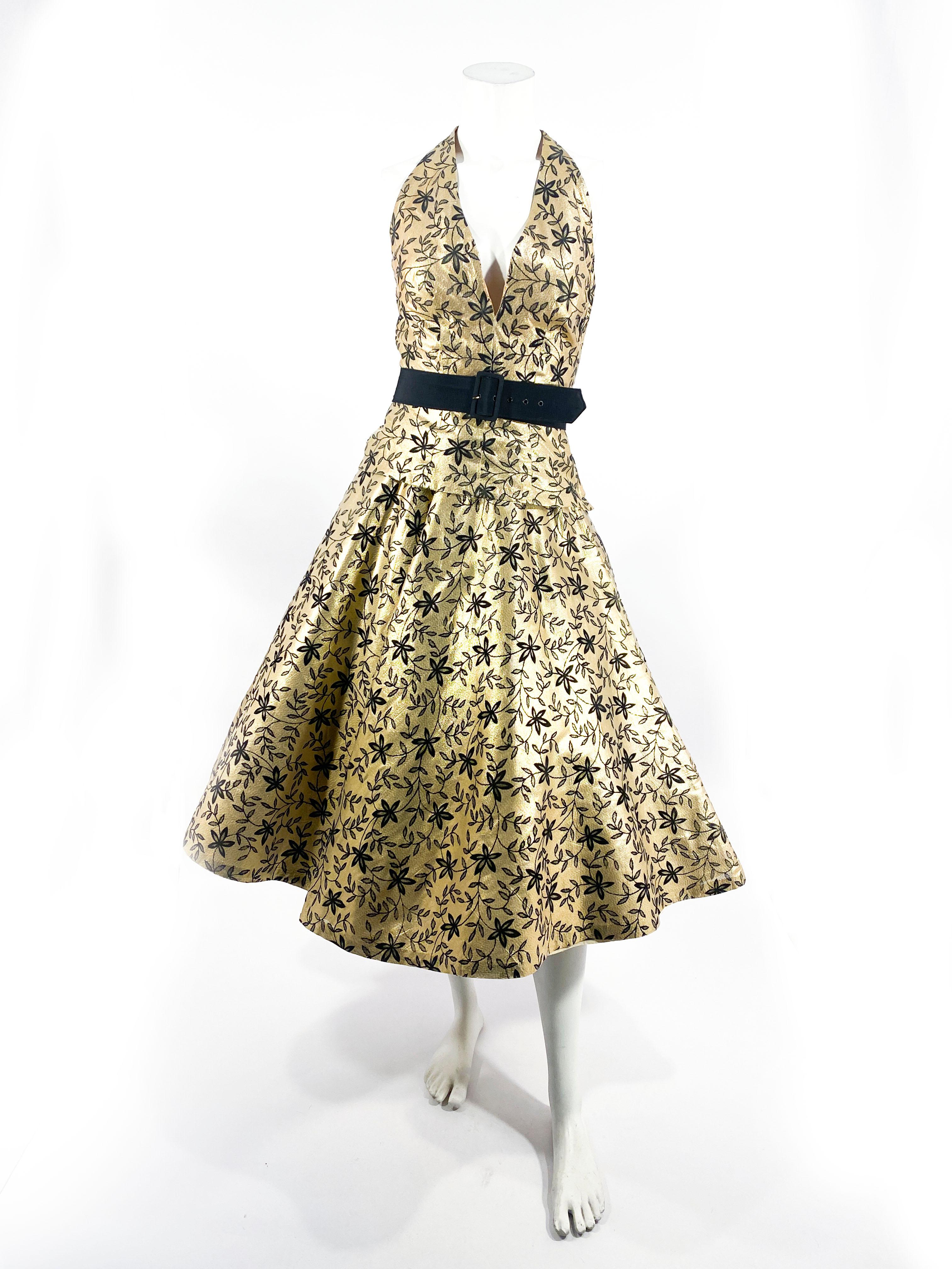 1950s custom-made two-piece cocktail dress made of a gold lamé with a black floral motif. The top has a deep plunge halter neckline and the back has a T-strap back detail. The top has a side sipper closure and the bottom of the top has a full