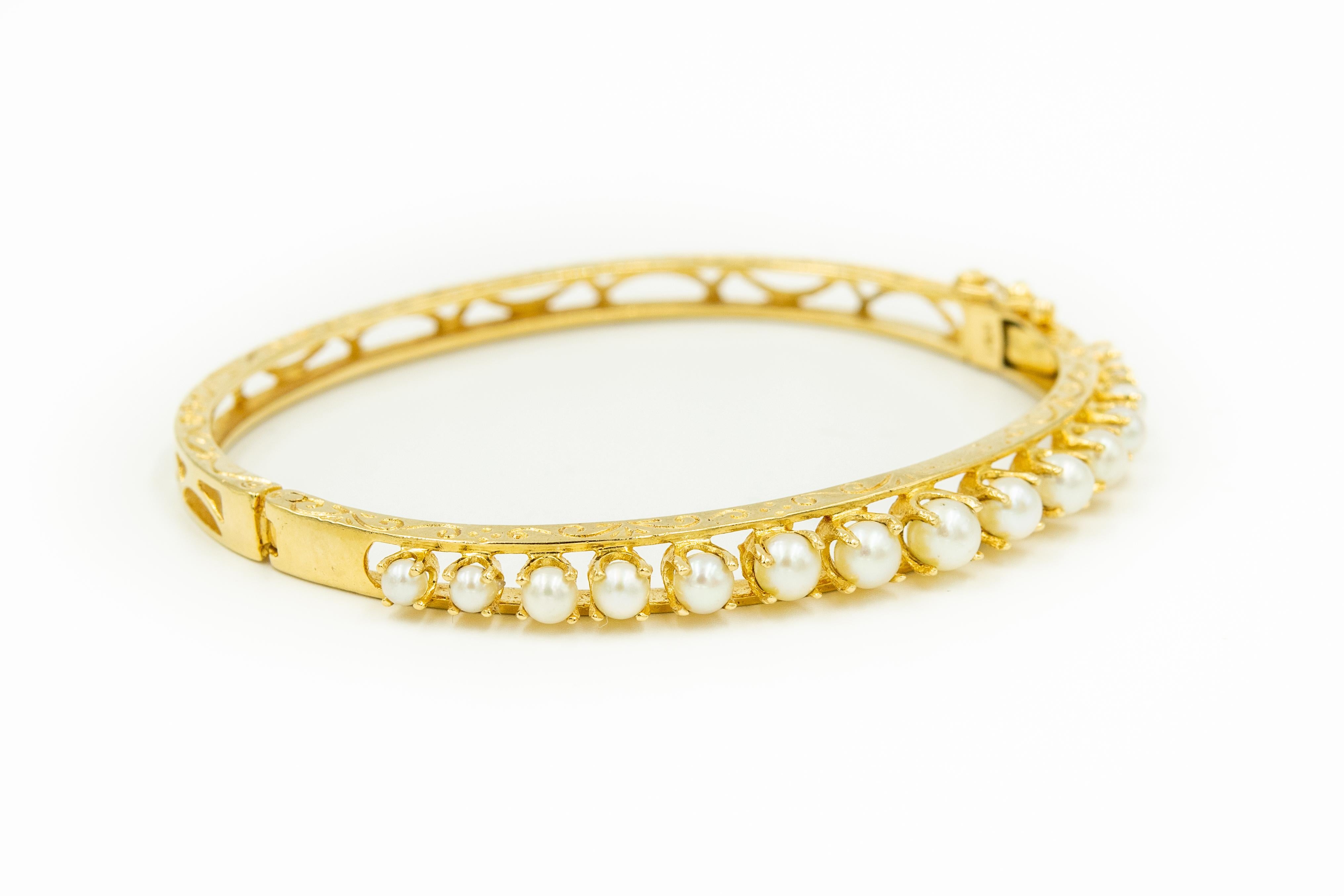 Classic 1950s elegant graduated cultured pearl bangle featuring 15 prong set cultured pearls (4.4mm-2.75mm) set in a 14k yellow gold bangle with etched scroll work along the top and bottom.  The back is pierced.  The bracelet hinges open and closes