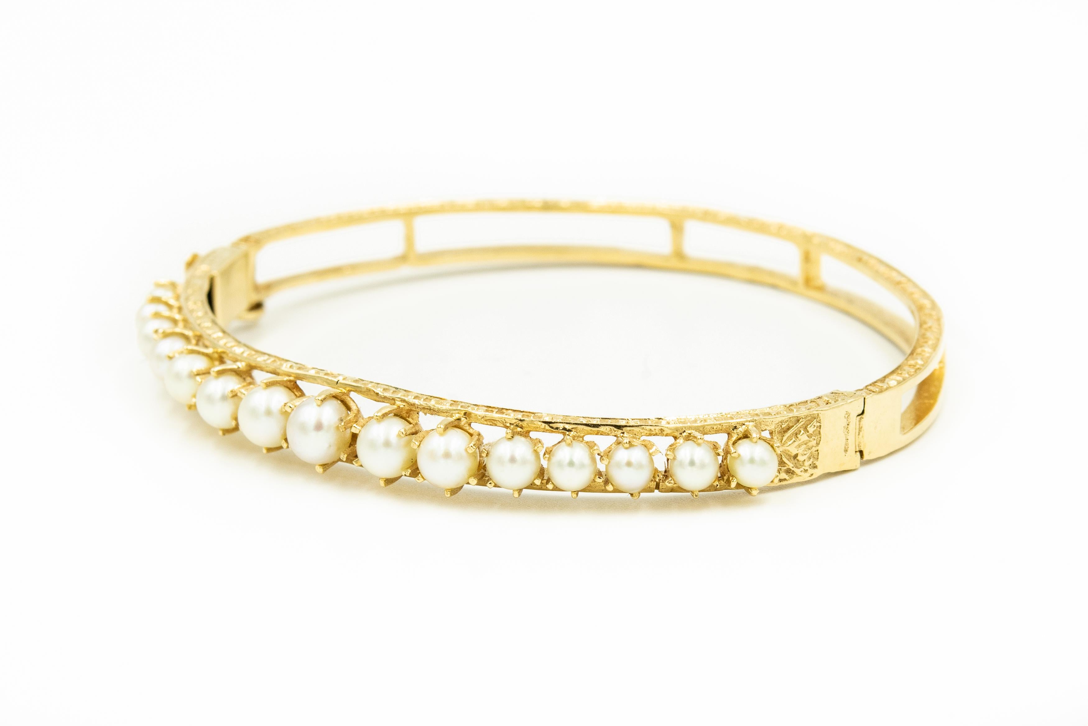 Classic 1950s elegant graduated cultured pearl bangle featuring 15 prong set cultured pearls (5.5mm - 3.7 mm) set in a 14k yellow gold bangle with etched sides.  The back is open.  The bracelet hinges open and closes with a push button clasp and an