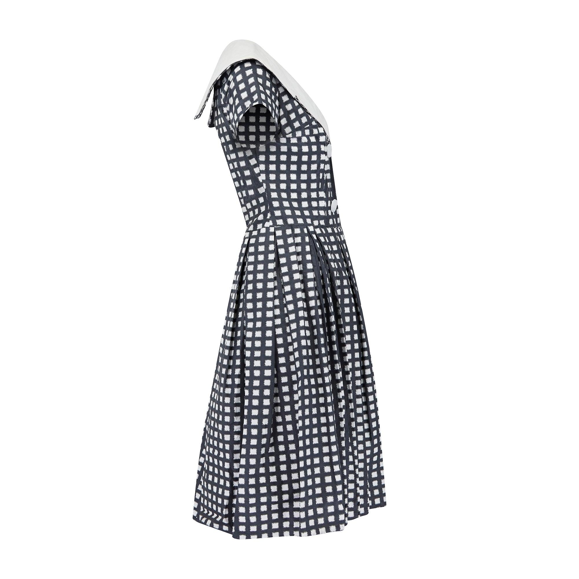 This late 1950s dress showcases many of the era’s fashionable hallmarks. We love the faux double-breasted front with chunky white plastic buttons and the boat neckline. The nipped-in waist and pleated full-skirt create the classic, highly feminine