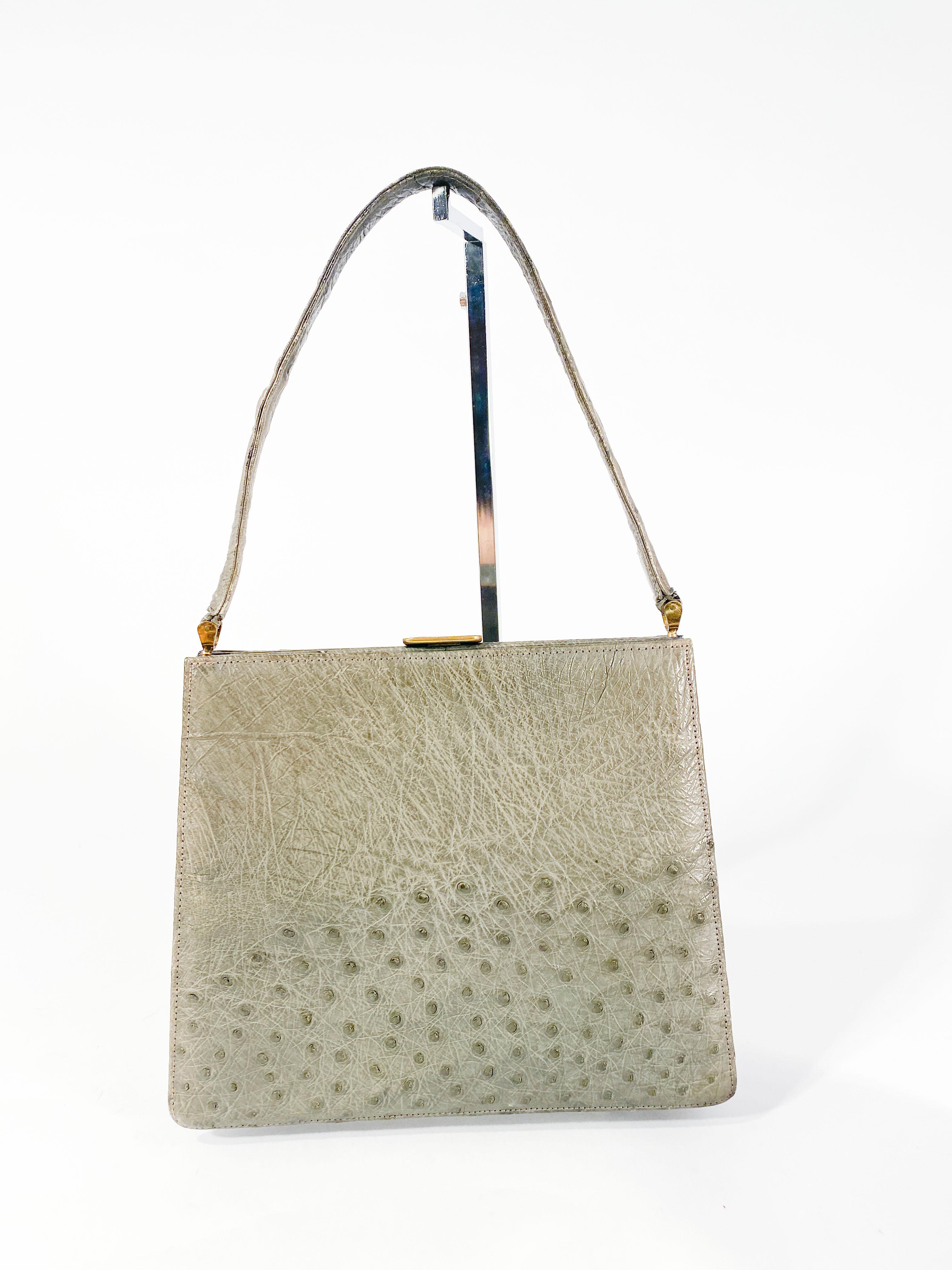 1950s Grey ostrich envelope handbag with matching top handle. The body of the bag is lined in suede with one large zip pocket and two open pockets for makeup and the included mirror. The clasp closure is made of brass finished with a small panel of
