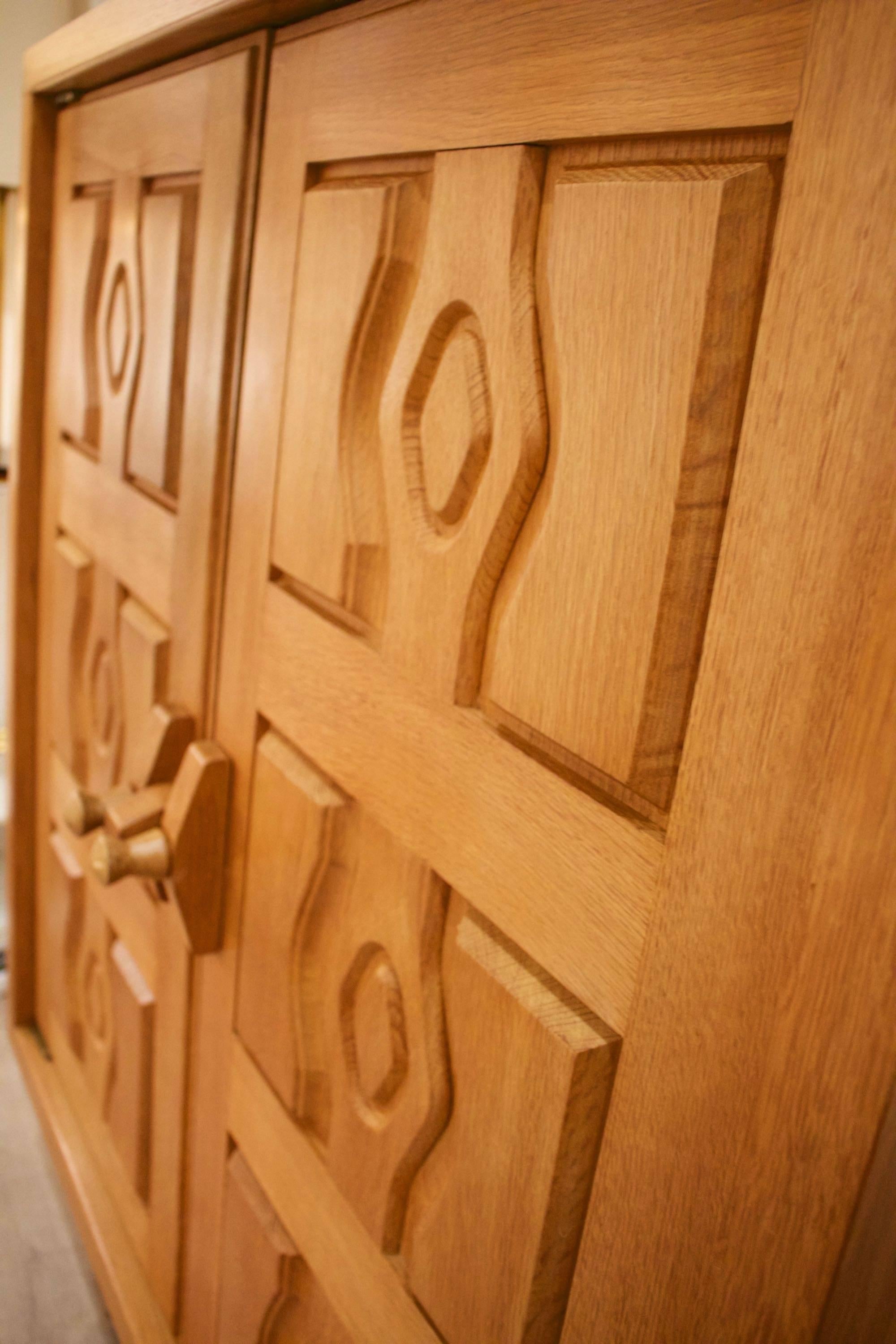The cabinet is in solid oak, it rests on 4 square section legs connected by a spacer.
Two opening doors adorned with geometric patterns and beautifully crafted door handles, typical of Guillerme and Chambron creations.
It opens onto a large storage