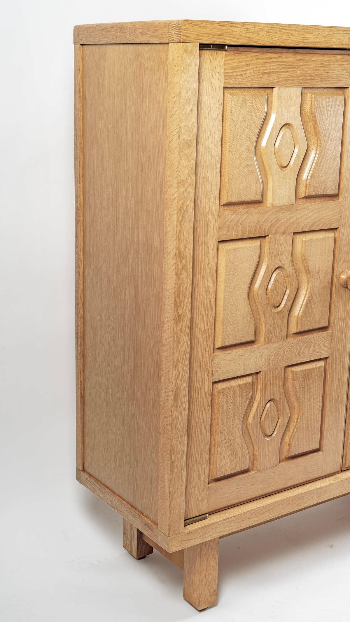 Solid oak cabinet by Guillerme and Chambron from the 1950s.

The four square-section legs support a large storage cabinet with two opening doors adorned with geometric patterns and ball handles with an ingenious locking system typical of Guillerme