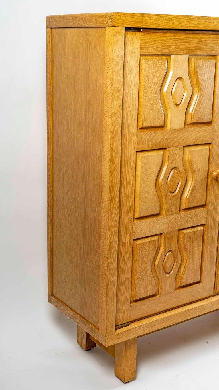 Armoire en chêne massif Guillerme et Chambron des années 1950.

Les quatre pieds à section carrée soutiennent un grand meuble de rangement à deux portes ouvrantes ornées de motifs géométriques et de poignées boules avec un ingénieux système