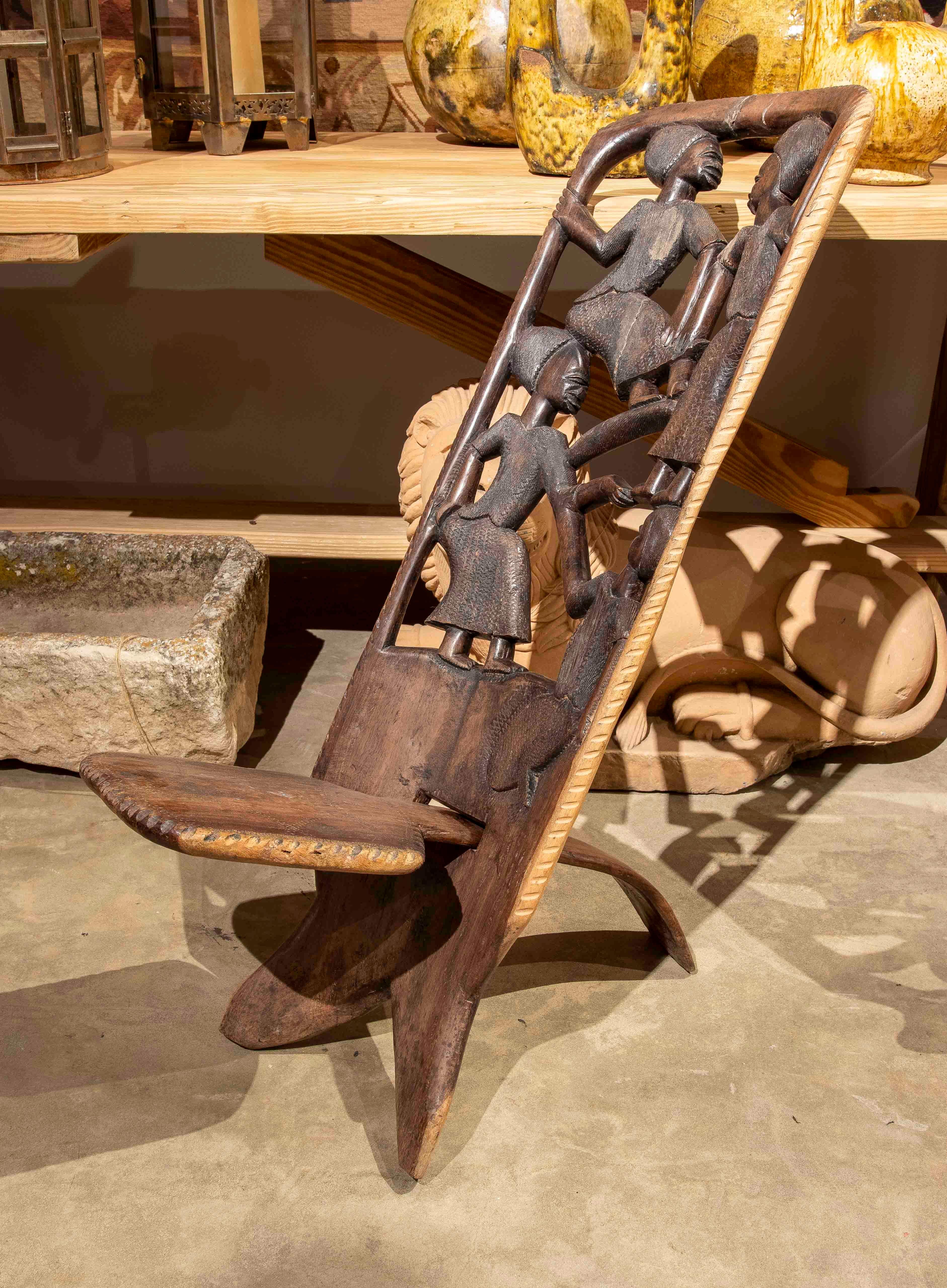 Questa sedia in legno lavorata a mano è un'opera d'arte unica, intagliata in modo intricato con scene che raffigurano figure umane in interazione, evocando i valori della comunità e della tradizione culturale. Il suo design dettagliato e simbolico