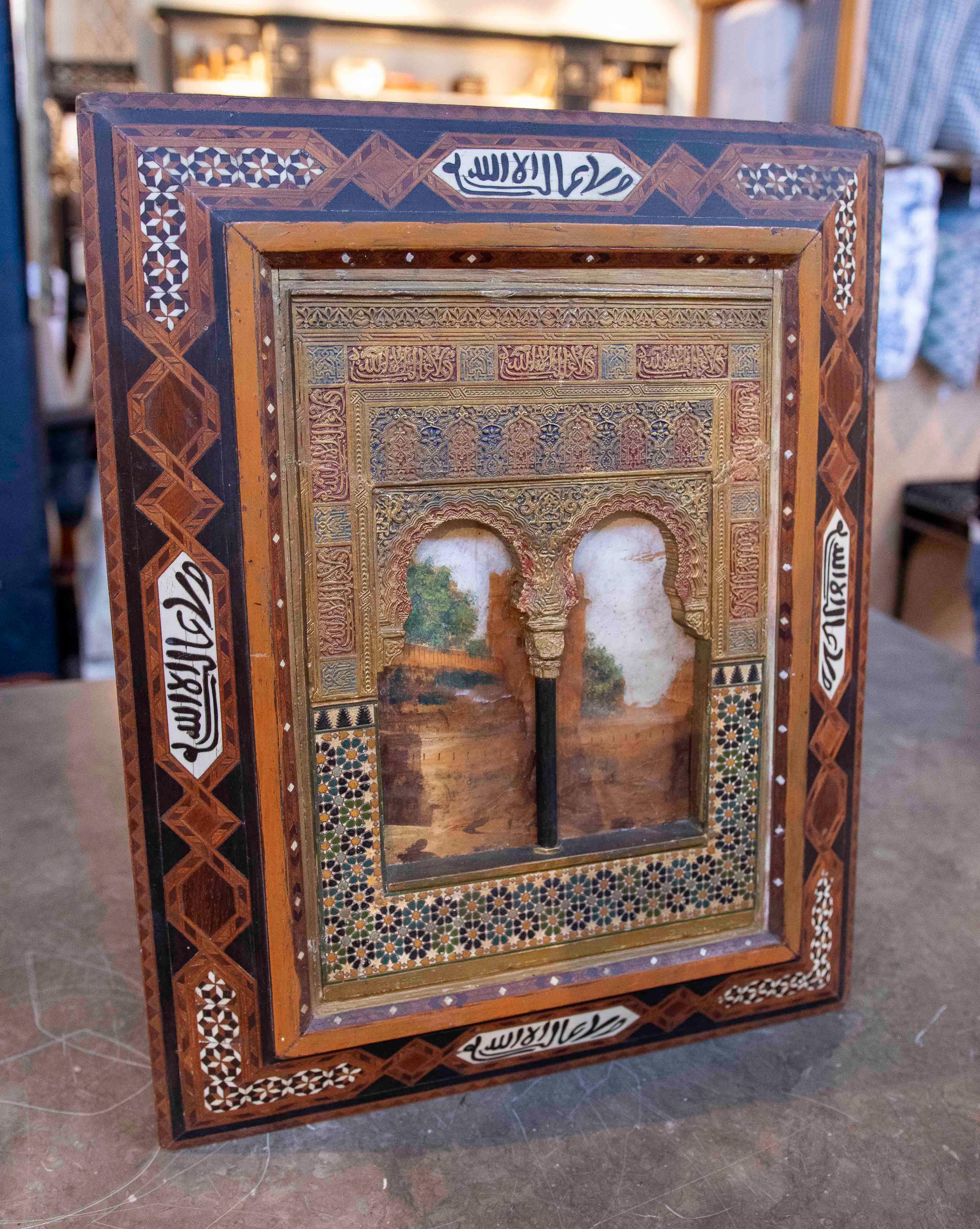 Exquis panneau décoratif inspiré de l'architecture de l'Alhambra de Grenade, avec marqueterie de bois détaillée et éléments dorés. La pièce présente deux arcs surélevés sur fond de paysage peint, entourés de motifs géométriques complexes et de