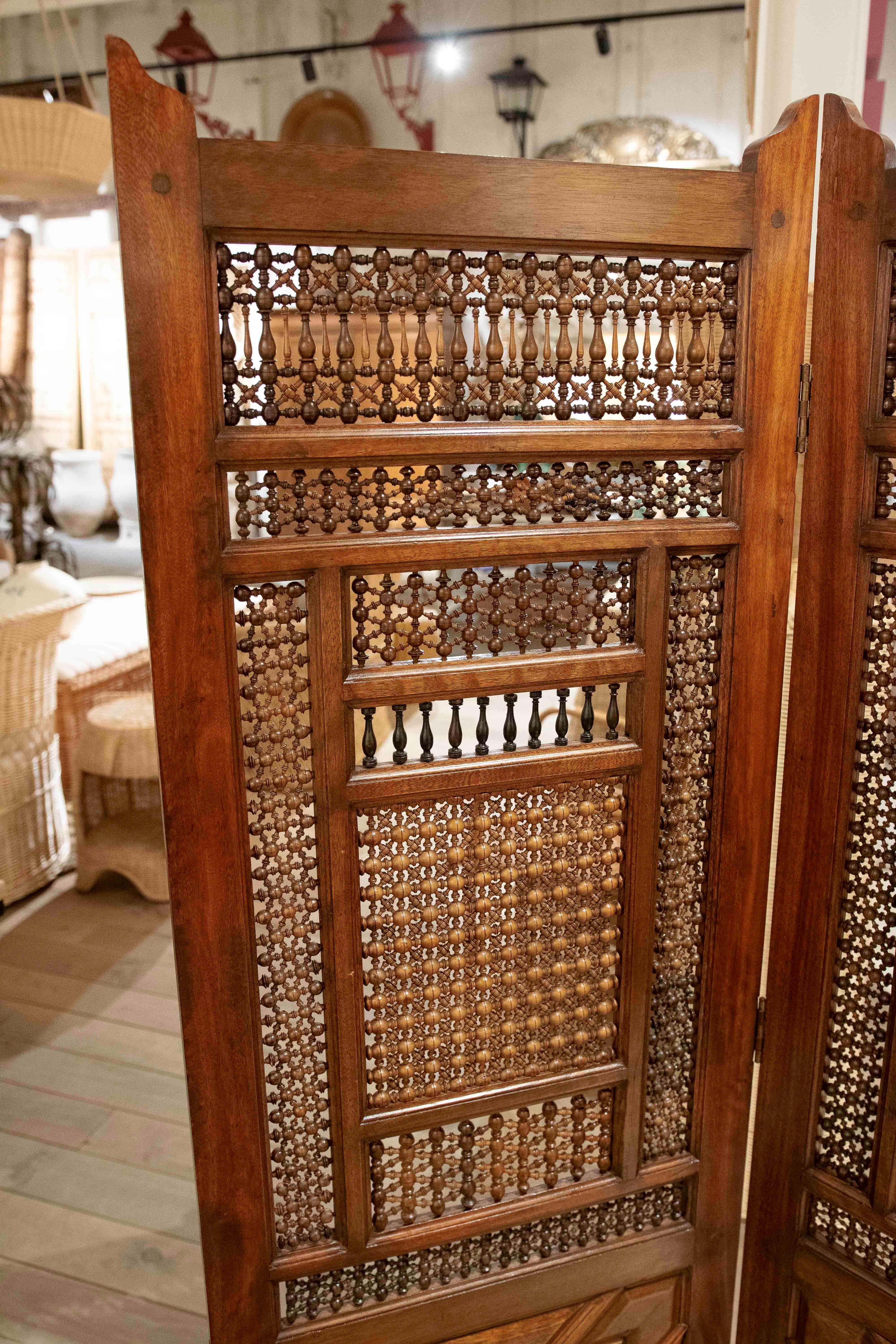 Elegante paravento in legno massello di Siria con un design meticolosamente intagliato a mano, composto da tre pannelli decorati con reticoli geometrici e dettagli torniti. Il suo stile combina influenze arabe e coloniali, permettendo una