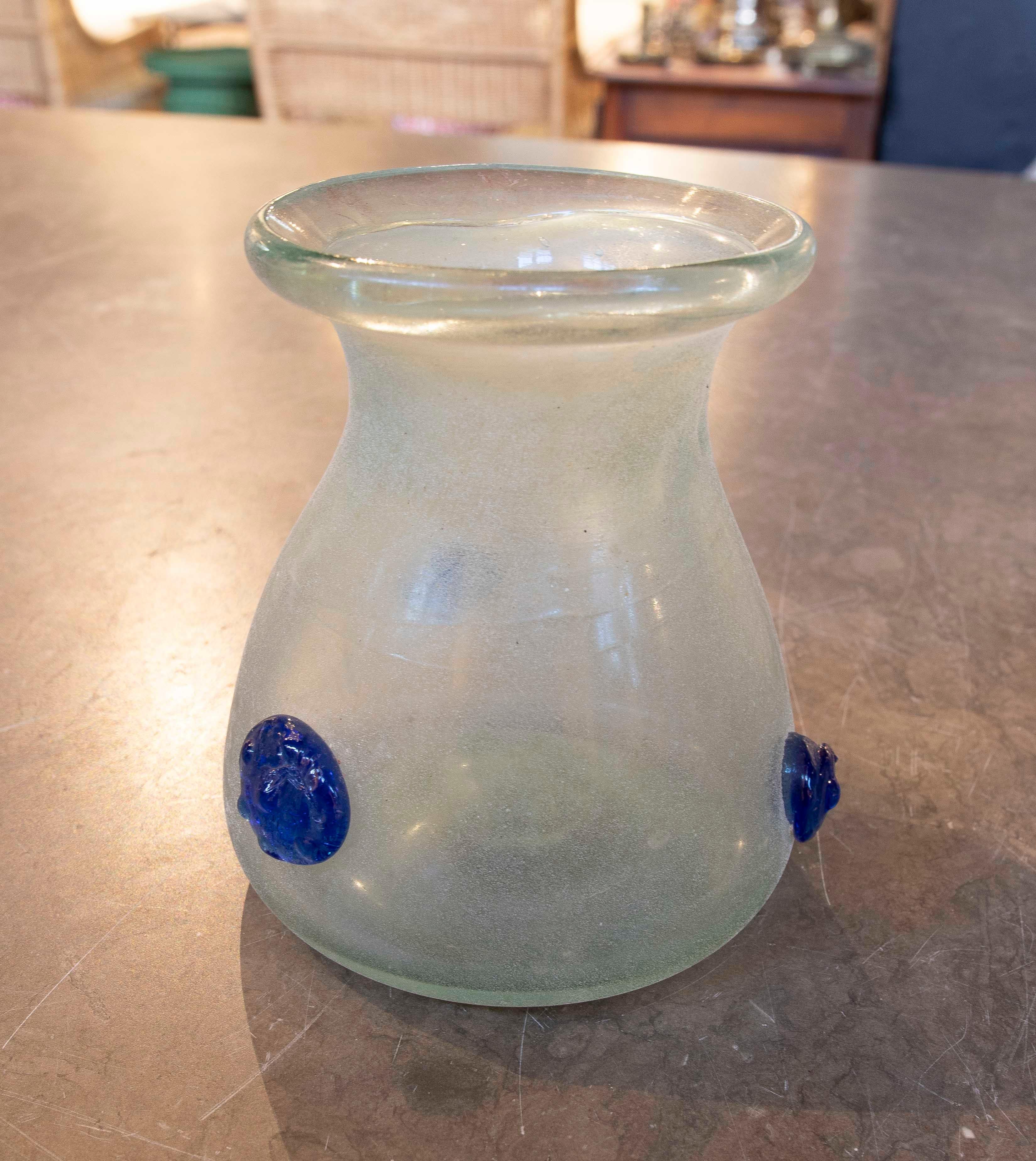 Vaso in vetro soffiato a mano di Murano, dal design minimalista che combina la trasparenza del vetro smerigliato con dettagli in rilievo di colore blu intenso. La sua forma a cupola e il collo stretto la rendono ideale per arredare qualsiasi spazio