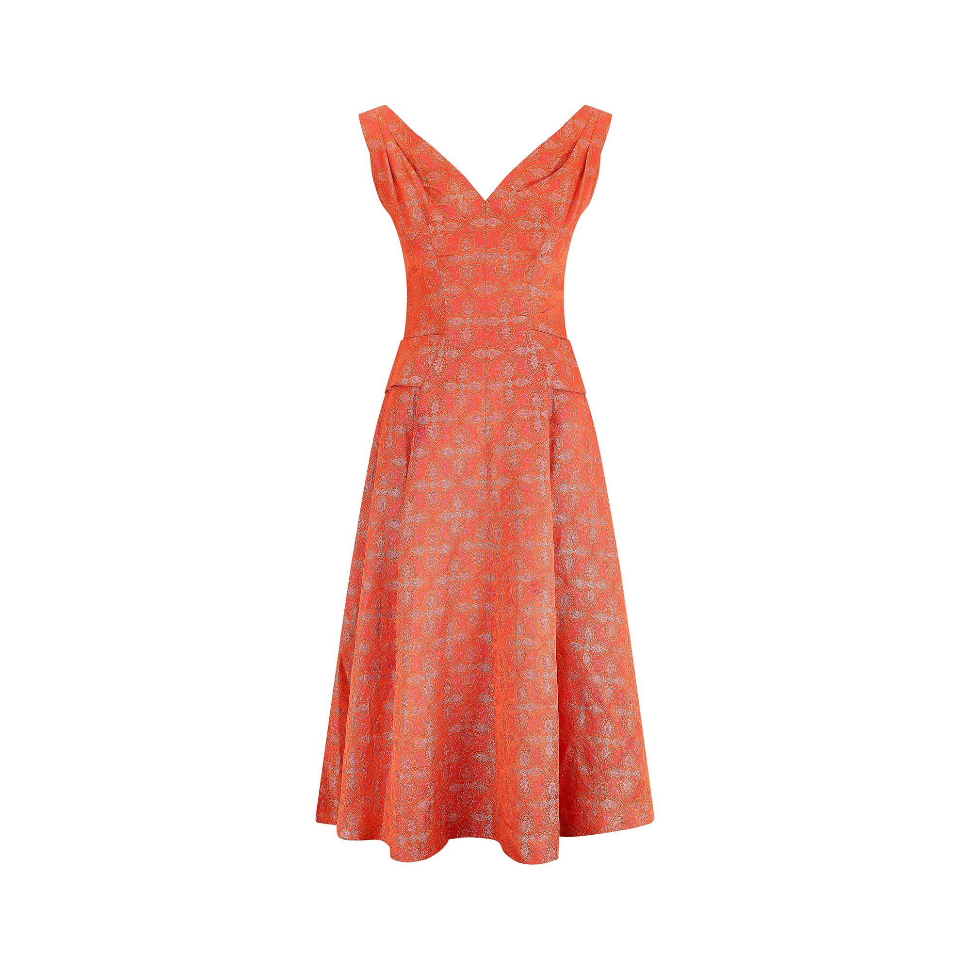 This mid 1950s Hardy Amies demi-couture occasion dress is made from a sumptuous material in a deep orange paisley brocade with pink and golds accents. It has a sweetheart neckline, pleated shoulders and fitted princess seams to really accentuate the