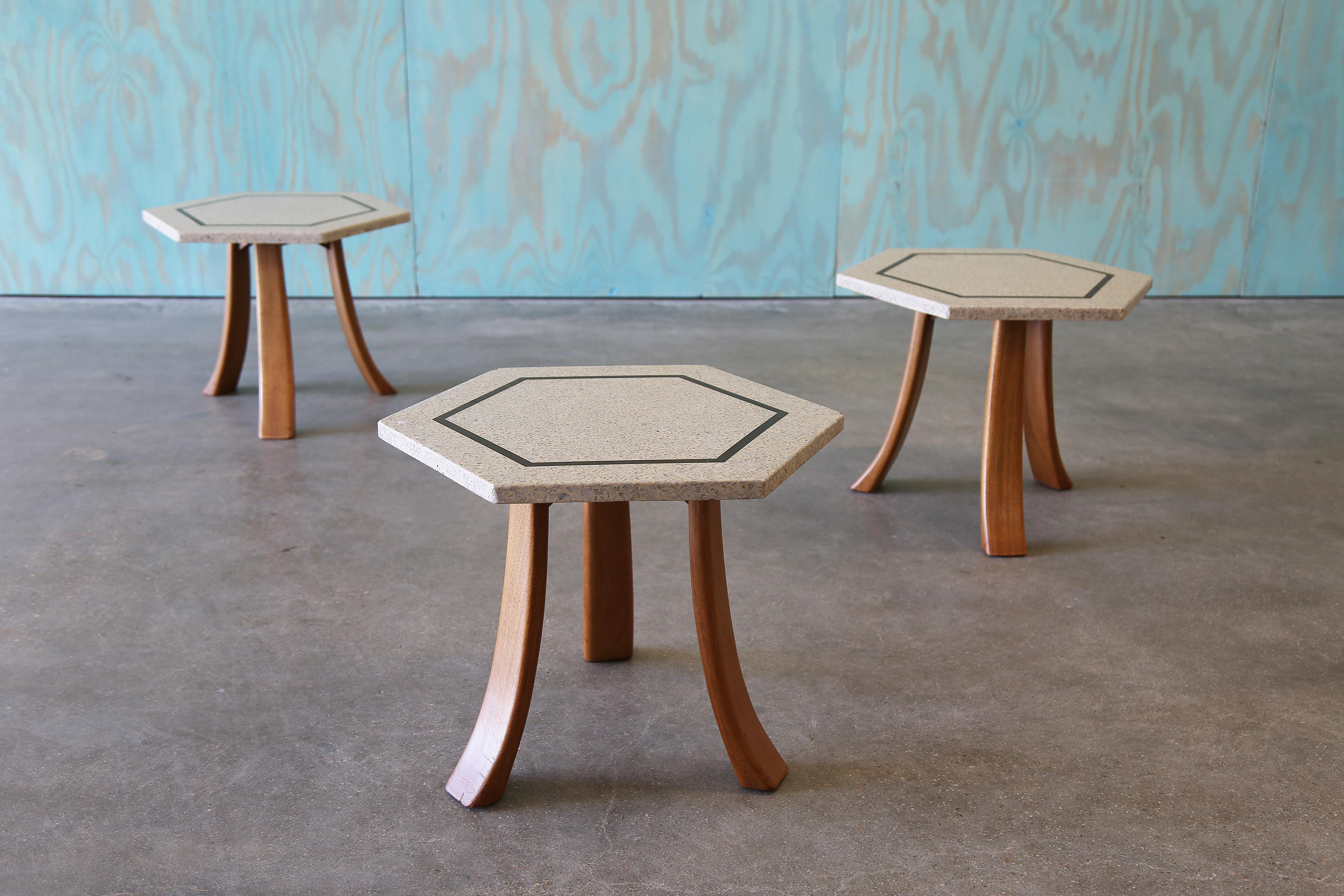 Rare ensemble de trois tables d'appoint hexagonales par Harvey Probber, A.I.C., USA, c. 1950s. Chaque pièce présente un plateau en terrazzo ivoire avec incrustation de laiton et des pieds sculpturaux en noyer incurvé. Ces tables peuvent facilement