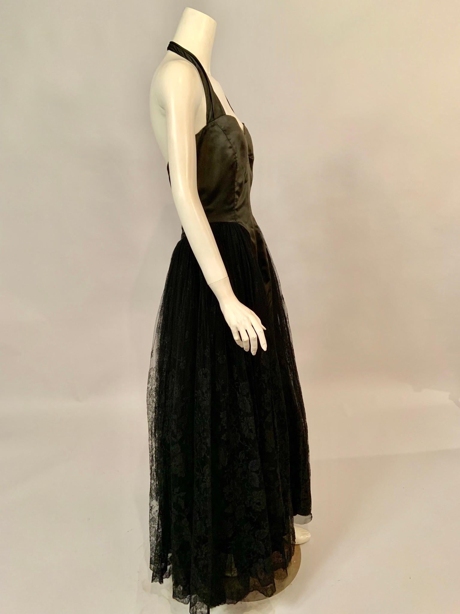 This black satin and lace halter neckline dress from Henri Bendel in New York City has a black satin bodice which runs seamlessly to the hemline at the center front and center back. The bodice is fully lined, boned and weighted at the interior