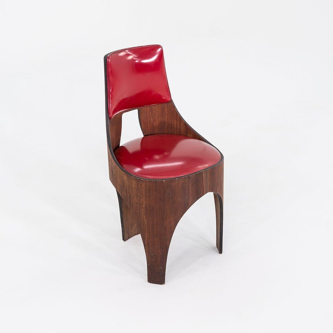 This is a Cylindra Dining Chair, originally designed by Henry P. Glass and produced by Richbilt Manufacturing Company in the 1950s. The chair is comprised of a walnut frame and has a seat upholstered in red vinyl. This particular example has veneer