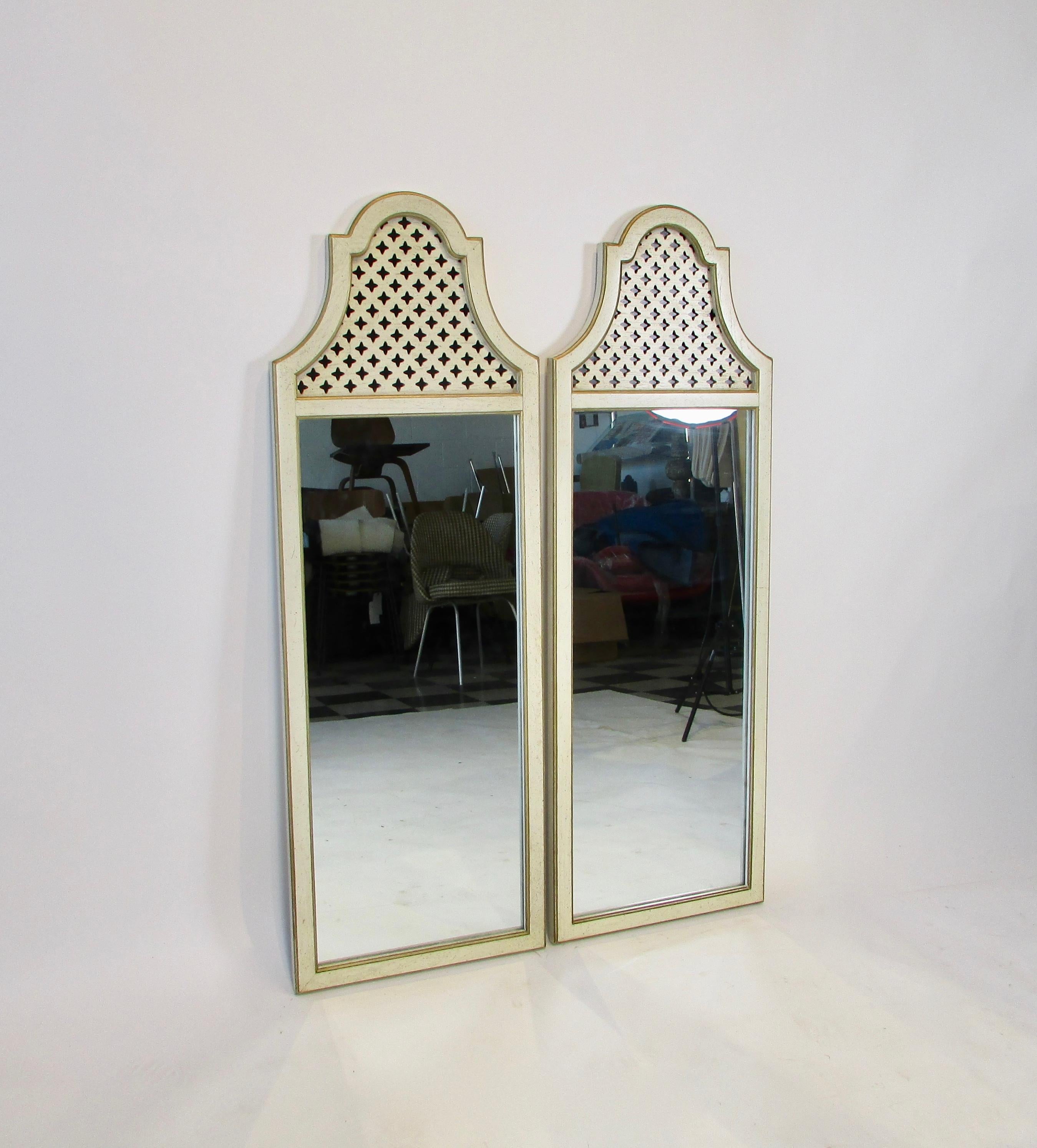 A pair of 1950s Hollywood Regency fretwork style wall mirrors. Creamy white with black speckled wood frames with gold trim outline and enhance the frames' shape. A star fretwork design reveals a black background.  These work well above a pair of