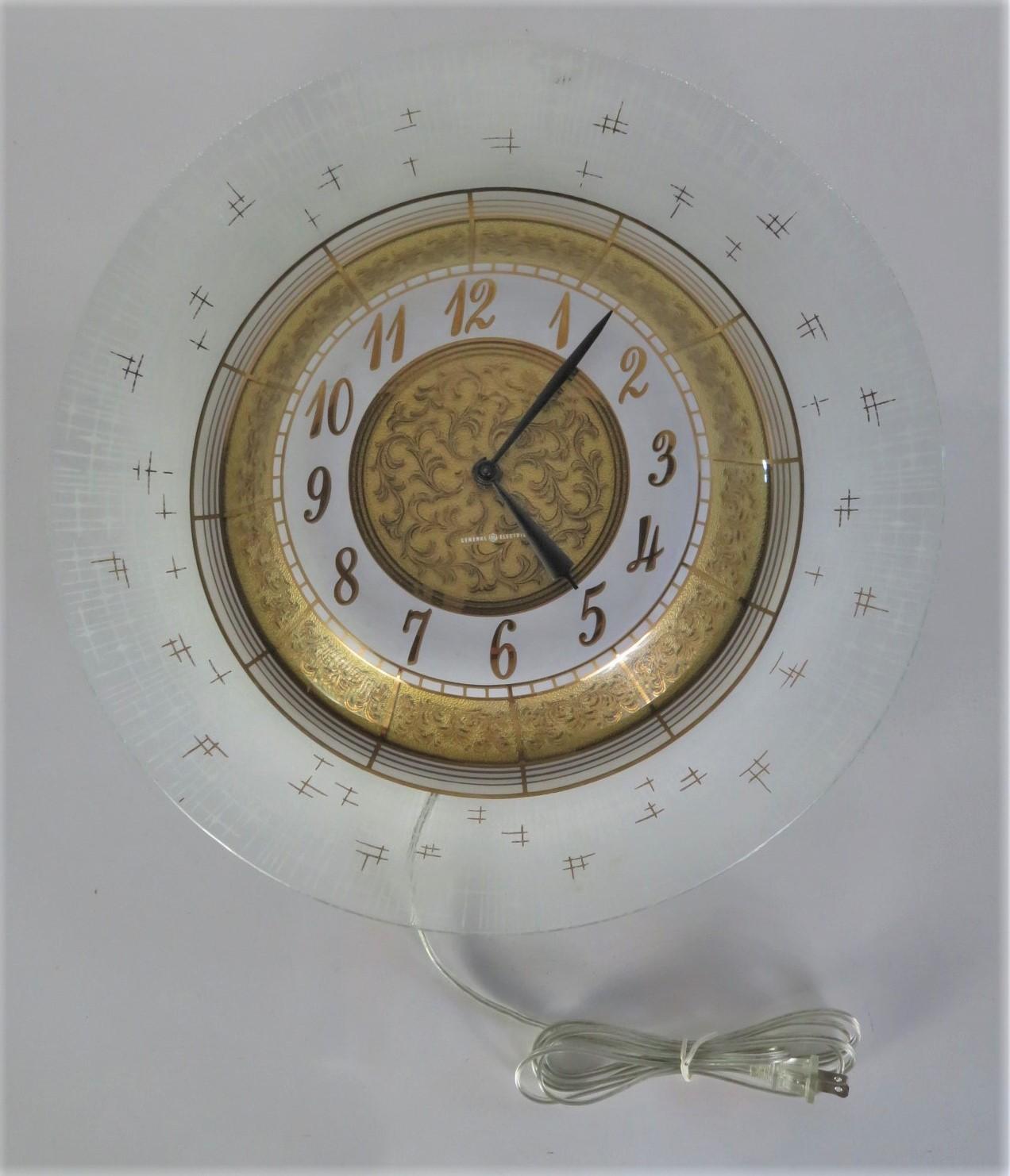 Modern and sophisticated, this Hollywood Regency and Higgins era glass bodied wall clock by General Electric has many decorative hallmarks starting with an undulating shape with gilt C scrolls to the inner areas on glass and a frosted stars streak