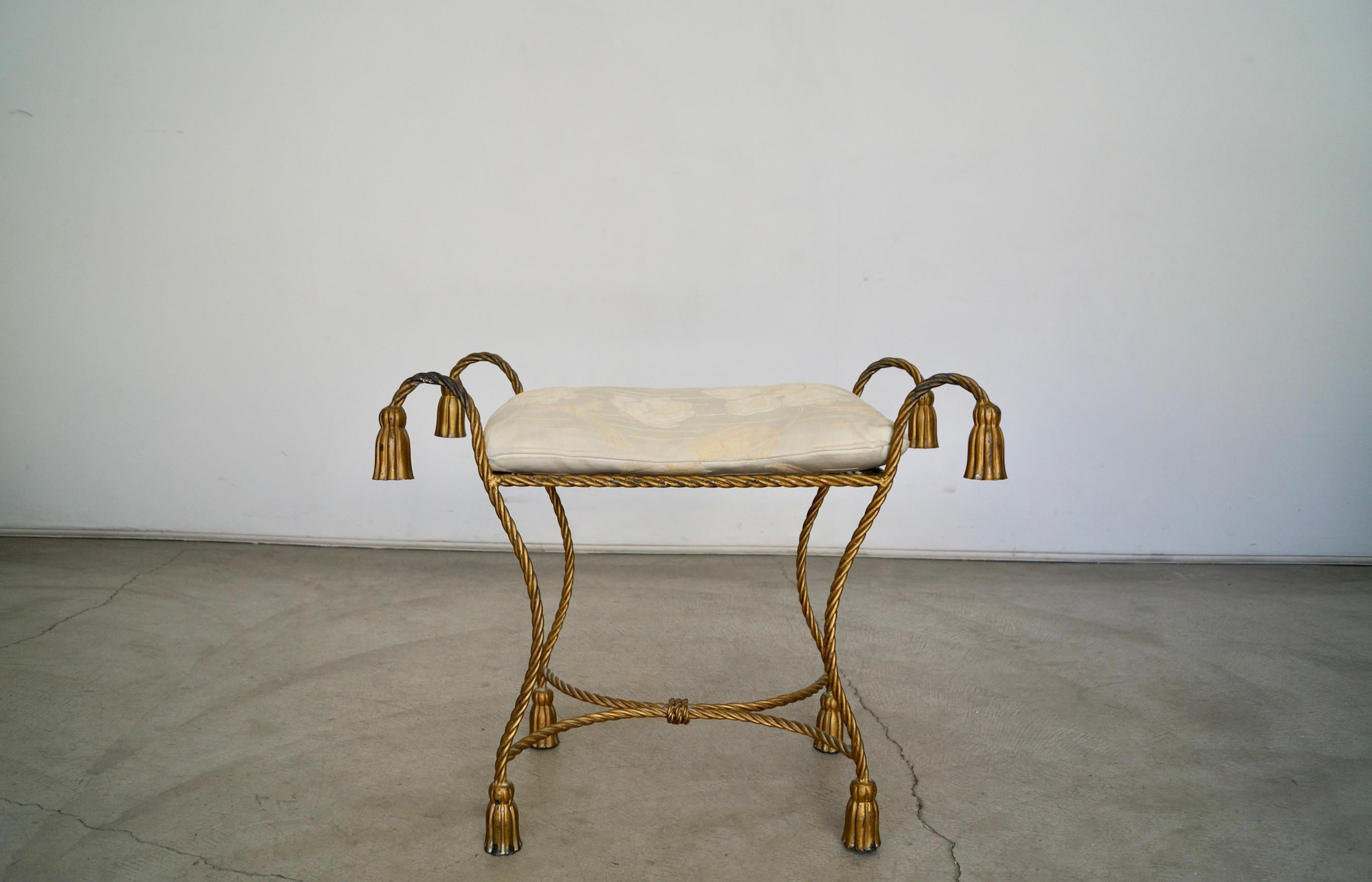 Vintage 1950s Hollywood Regency vanity stool bench for sale. Made of metal with a gold aged brass finish and beautiful patina. Tassel rope design with tassel rope legs. Wonderful metal work with great texture. Has a loose cushion in excellent