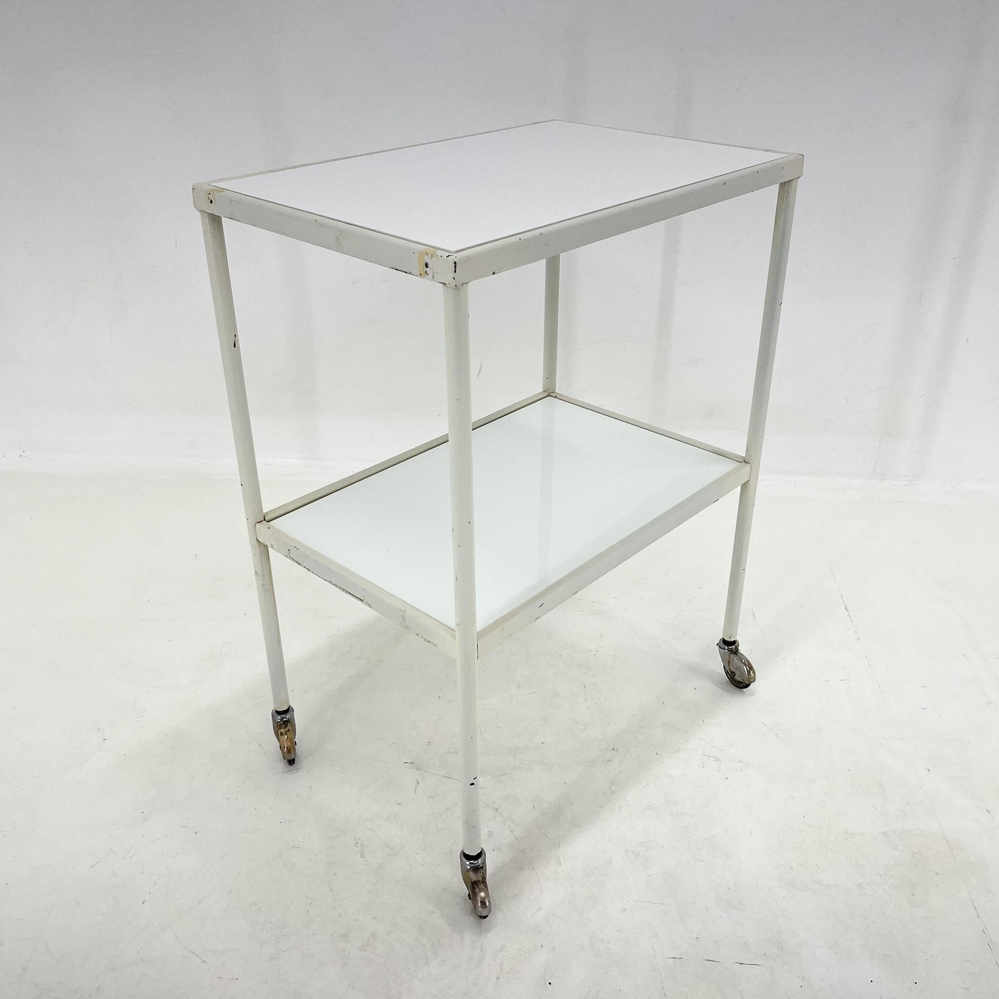 Mesa o carro médico vintage con pátina original. El estante inferior es original, de cristal opaco. La superficie superior se sustituye por un tablero blanco de plástico endurecido.