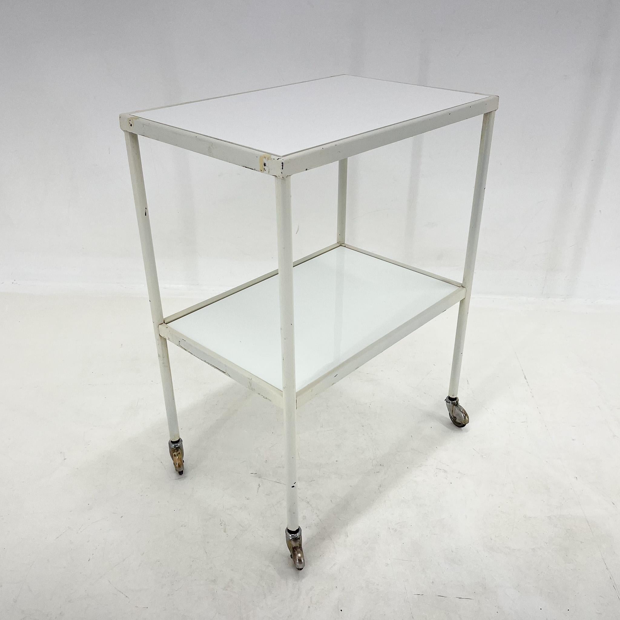 Vintage medical table or trolley with original patina. The bottom shelf is original, made of opaxite glass. The top surface is replaced by a white hardened plastic board.