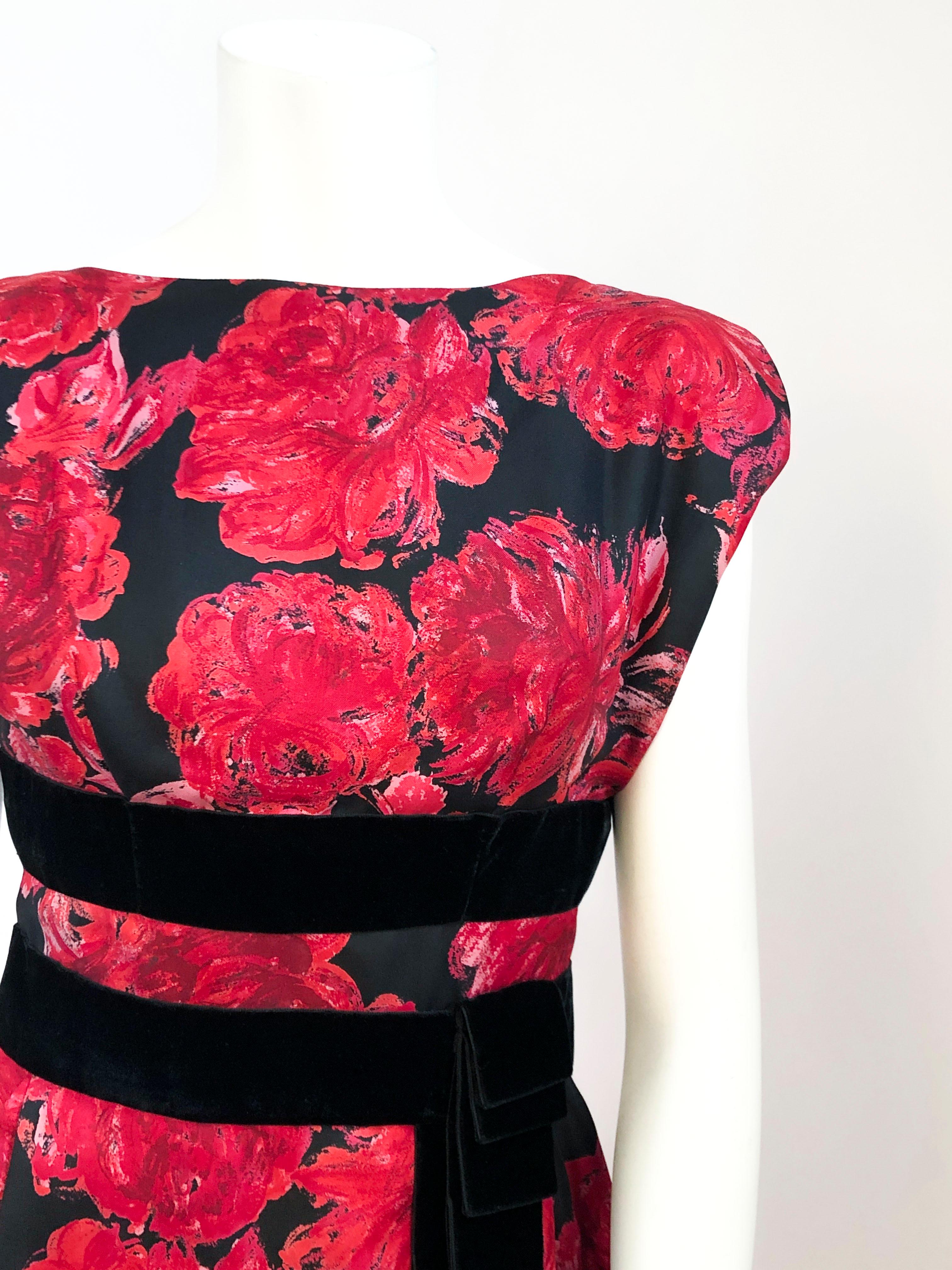 Silk dress with an impressionistic red-toned floral print with black fore-color. The waist is extenuated by dual applied strips of velvet that is finished with a layered, decorated flounce. It has a boat neck on the face of the dress and a low back