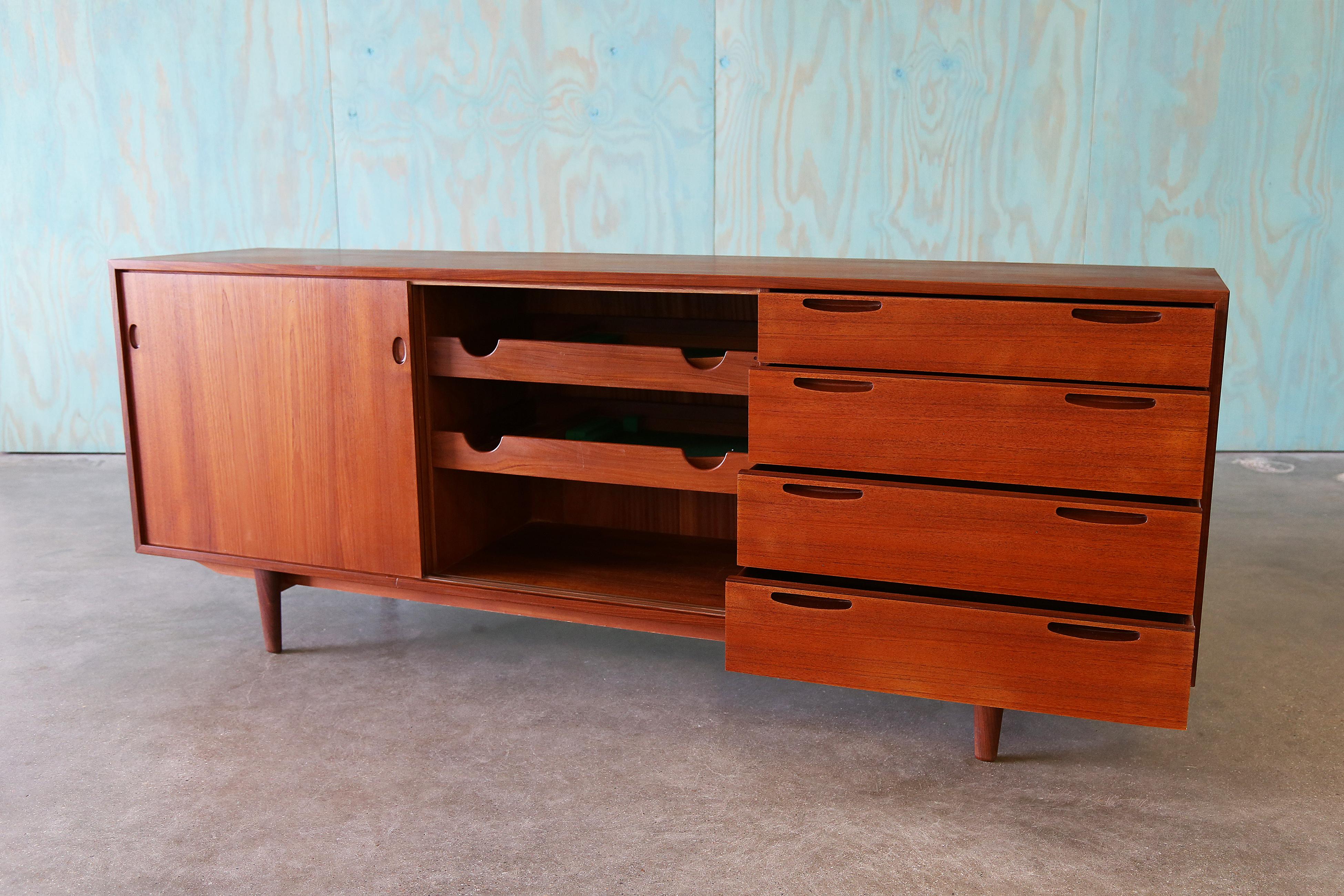 Ib Kofod Larsen for Clausen and Sons Denmark Teak Sideboard buffet. Iconic recessed handles access four drawers with unique box joinery. Sliding doors conceal two shelves for added storage.  Elevated on tapered legs.  Lighter Teak veneer is