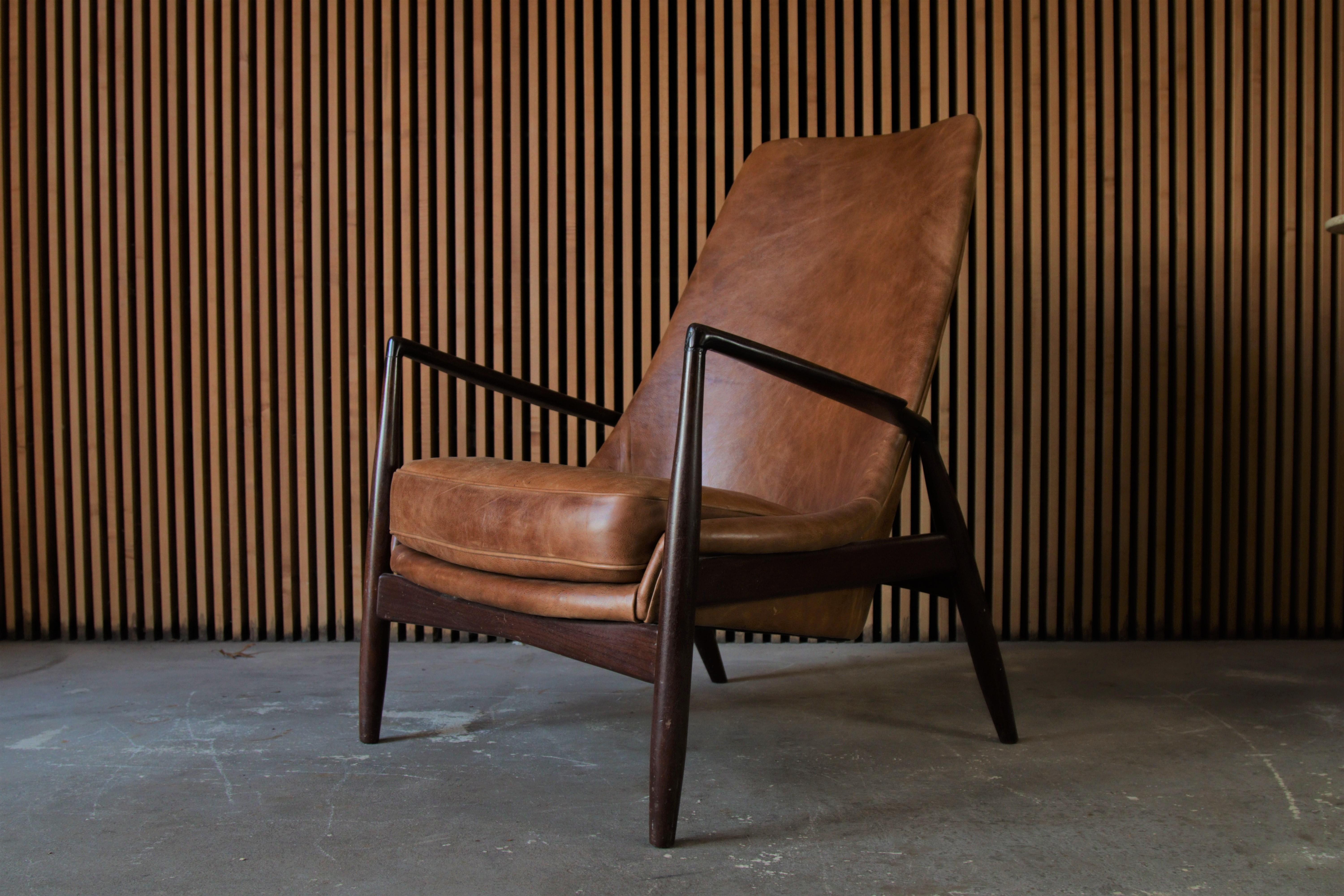 A vintage high back seal lounge chair designed by Ib Kofod-Larsen for Illums Bolighus. This example in Afromosia teak and distressed cognac leather. The Afromosia teak with a dark and rich patina.

Dimensions:
28