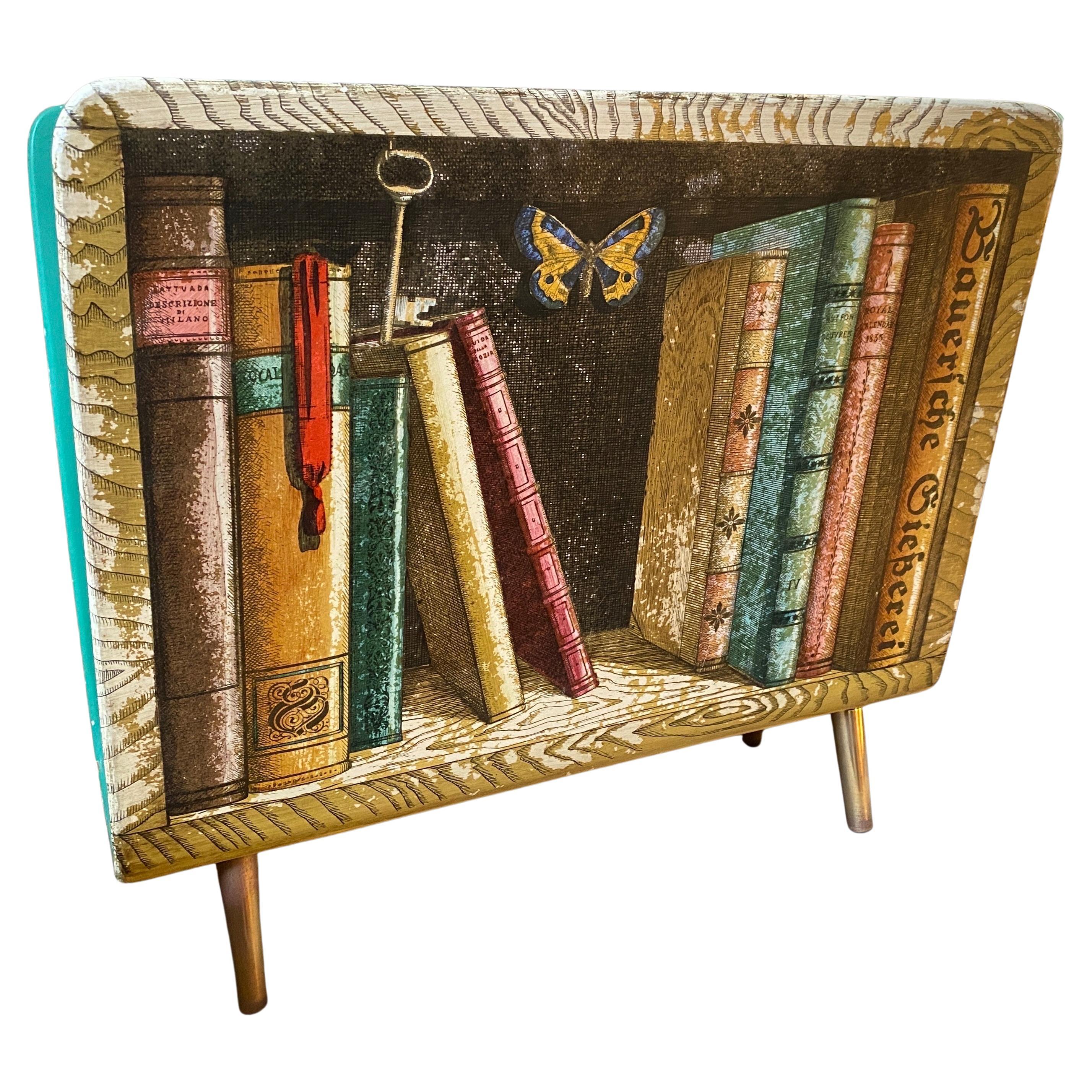 An amazing magazine stand designed by Piero Fornasetti and manufactured by Atelier Fornasetti in Milano in the 1950s. The vintage magazine stand is made of lithographically printed and lacquered plywood depicting an antique bookcasee. it has a brass