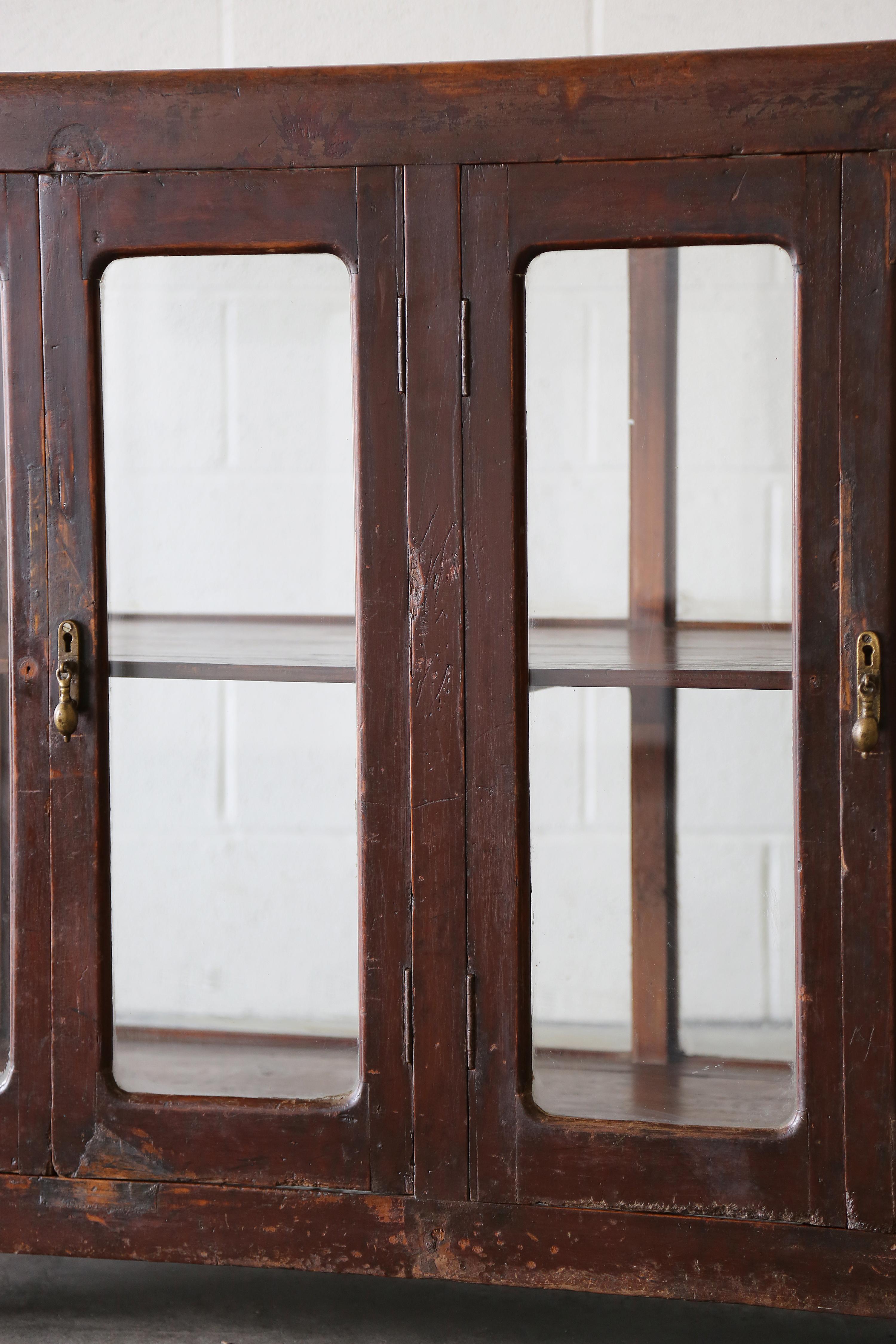Una vetrina in teak birmano importata dall'Indonesia. Grande patina e aspetto primitivo con ferramenta originale I pannelli di vetro su tutti i lati e la parte superiore rivelano un ripiano interno/ Può essere utilizzato come bar, vetrina, archivio