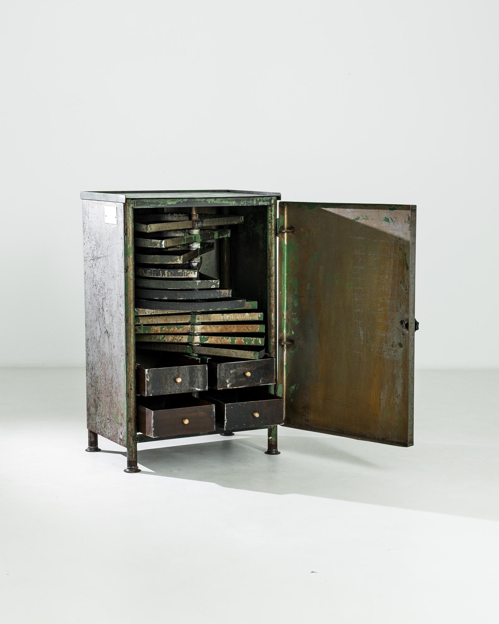Manufactured in Central Europe circa 1950, this industrial cabinet adopts a perfectly rectangular shape punctuated by short tubular legs. A wide metal door decorated with a minimalist black heptagon pull hides the intricate interior of iron