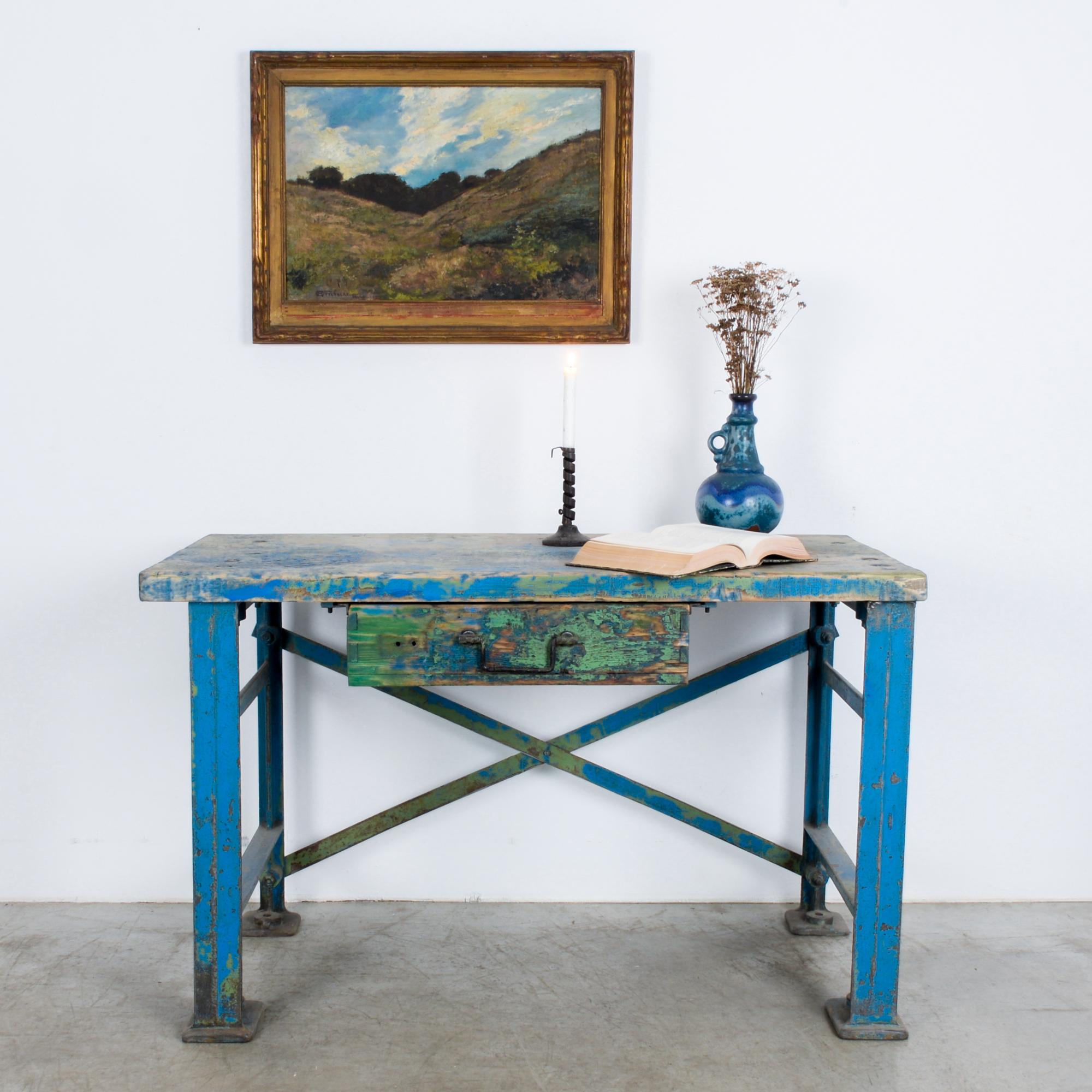This worktable was made in Central Europe, circa 1950. The table features a wooden tabletop and a drawer. Supported on metal posts with an X-frame back, this sturdy worktable evokes an industrial sensibility. The striking patina of the weathered