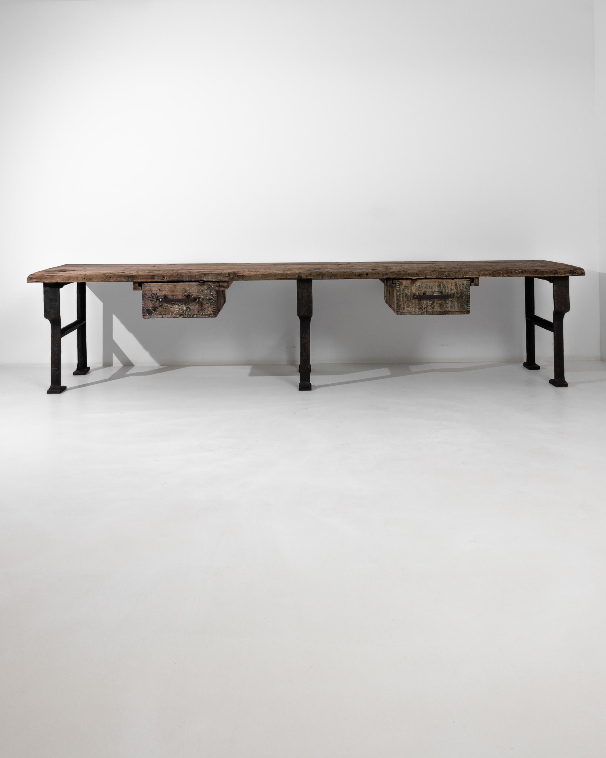 This work table built in Czechia circa 1950 is divided in two identical sections equipped with deep wooden drawers: their coarse metal handles mirror the iron A-shaped legs that support the table at the center and from the sides. The unrefined
