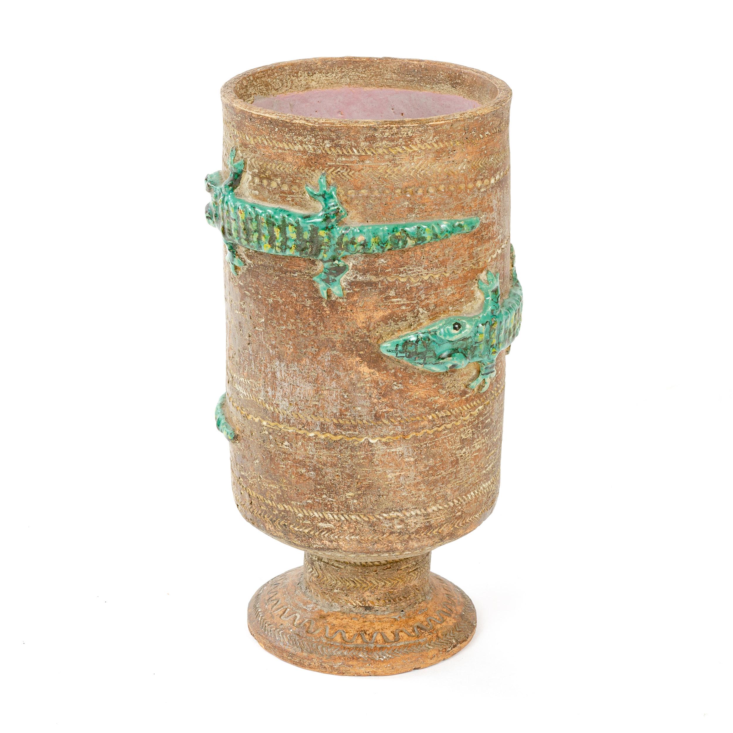 Tall, footed earth tone pottery vase with a rough, tactile surface treatment having raised alligators in a contrasting gloss green glaze ringing the upper body. Marked on its underside with the upper case initials 'D' and 'G' in gold lettering. Very
