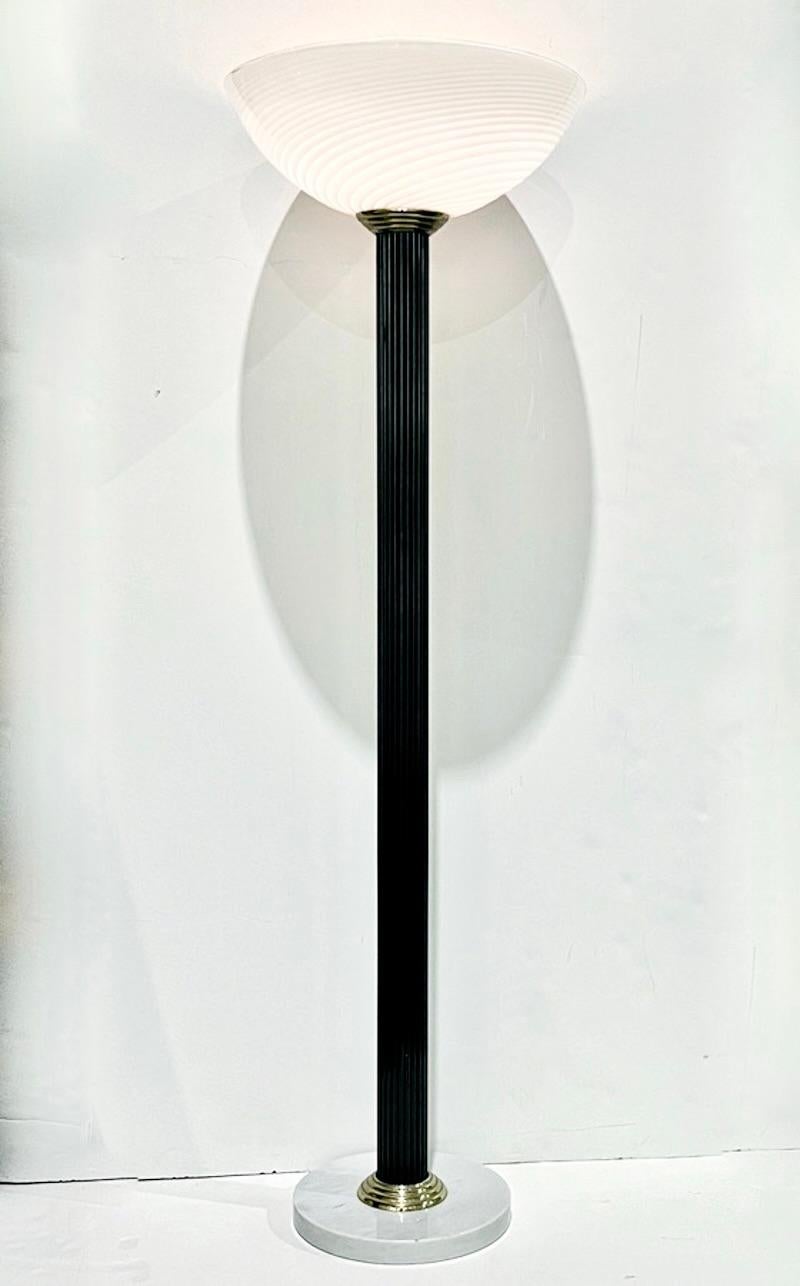 This mid-20th century Italian design Antique Art Deco style floor lamp, a creation entirely handcrafted in Italy with an iconic 1920s flared organic shape, is composed of a handmade stem in black lacquer reeded wood, supporting on a stepped brass