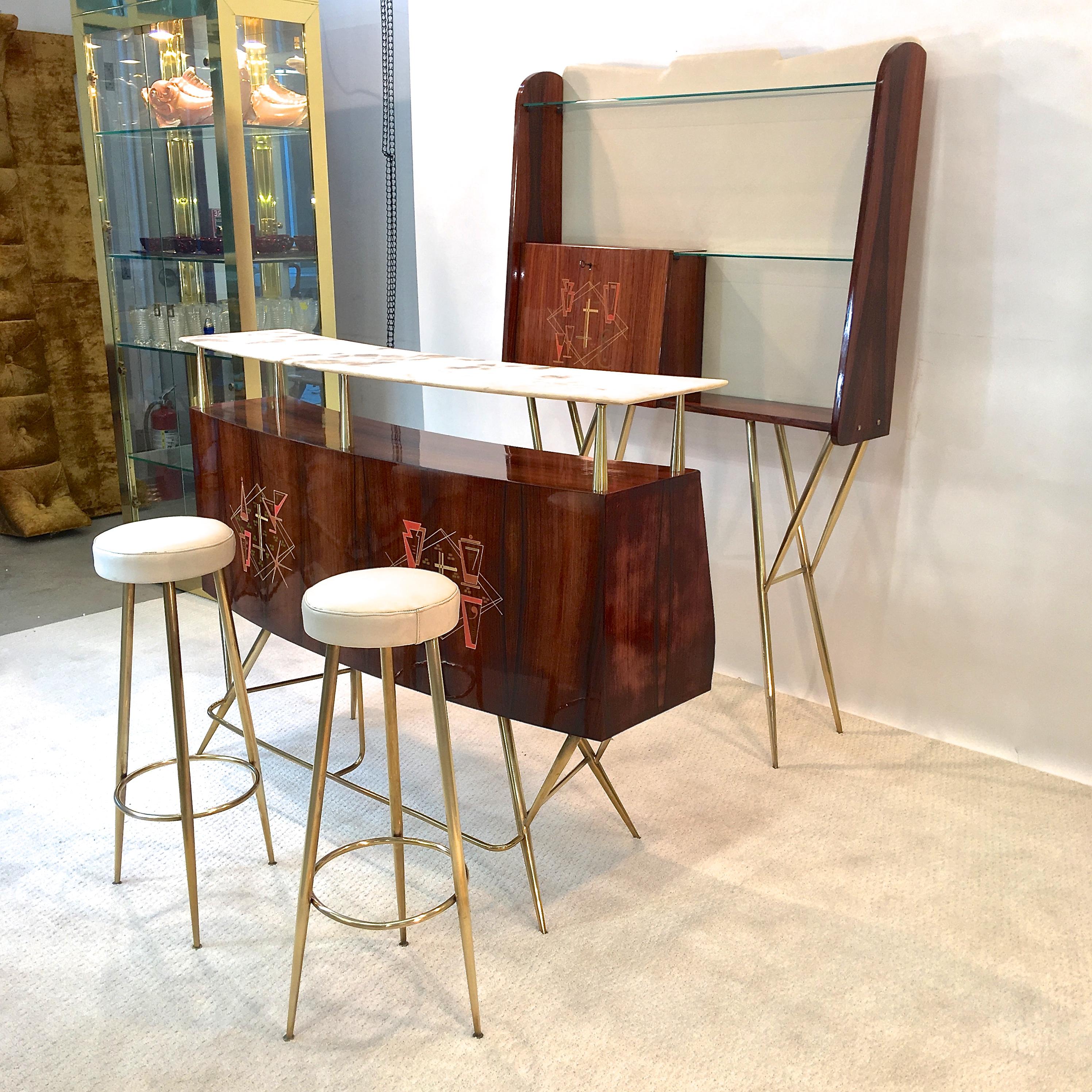 Exquisitely stylish 1950s Italian dry bar in rosewood and architectural tapered brass supports with floating curved marble top above a curved rosewood case inlayed with period cocktail motif graphic, open bottle storage on the backside and a single