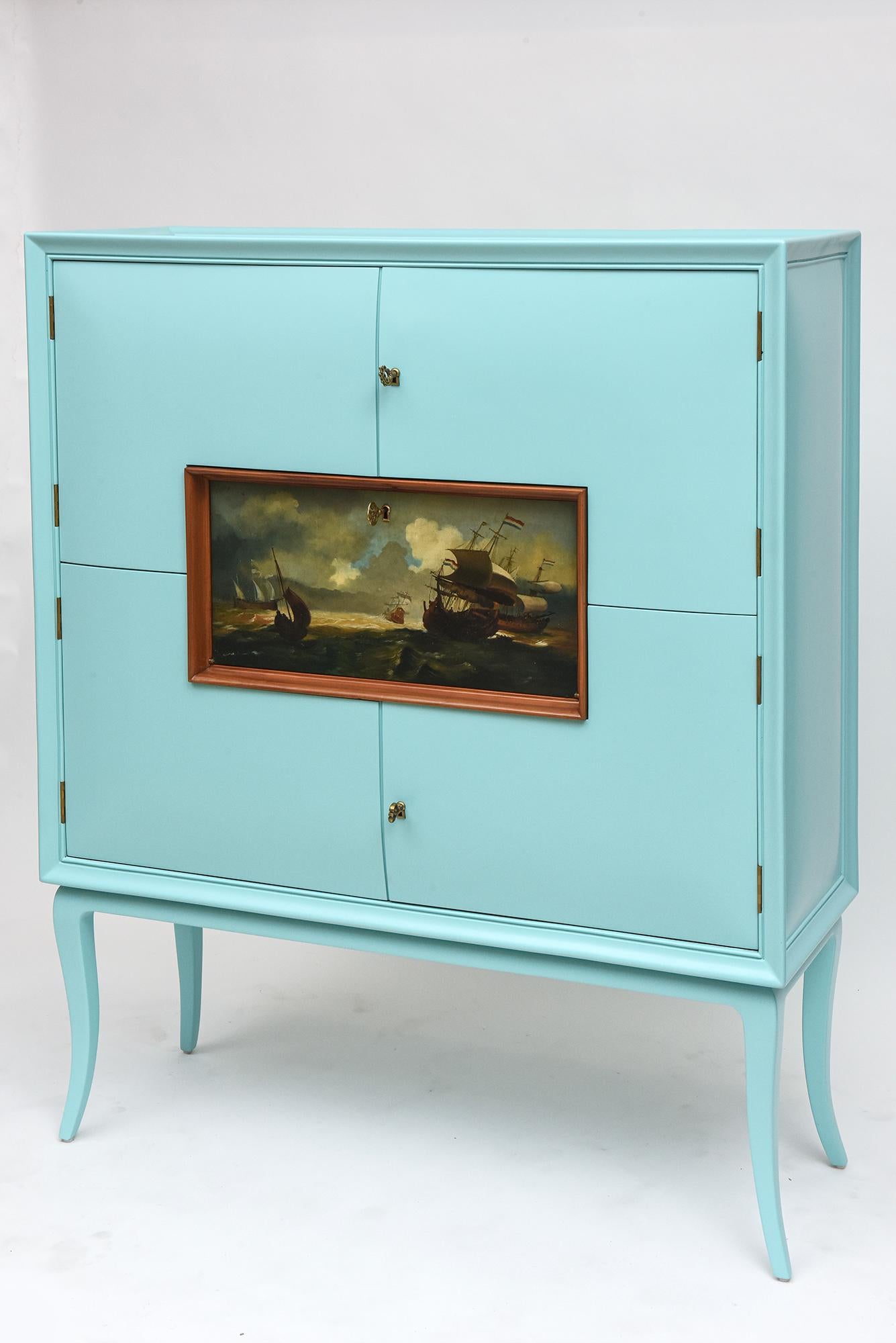 Dramatic 1950s Italian bar cabinet features an elegant curved body on tall, slender cabriole legs, gessoed and painted in Tiffany box blue and lined in rich European walnut. Center framed fold-down shelf features a classical maritime oil painting