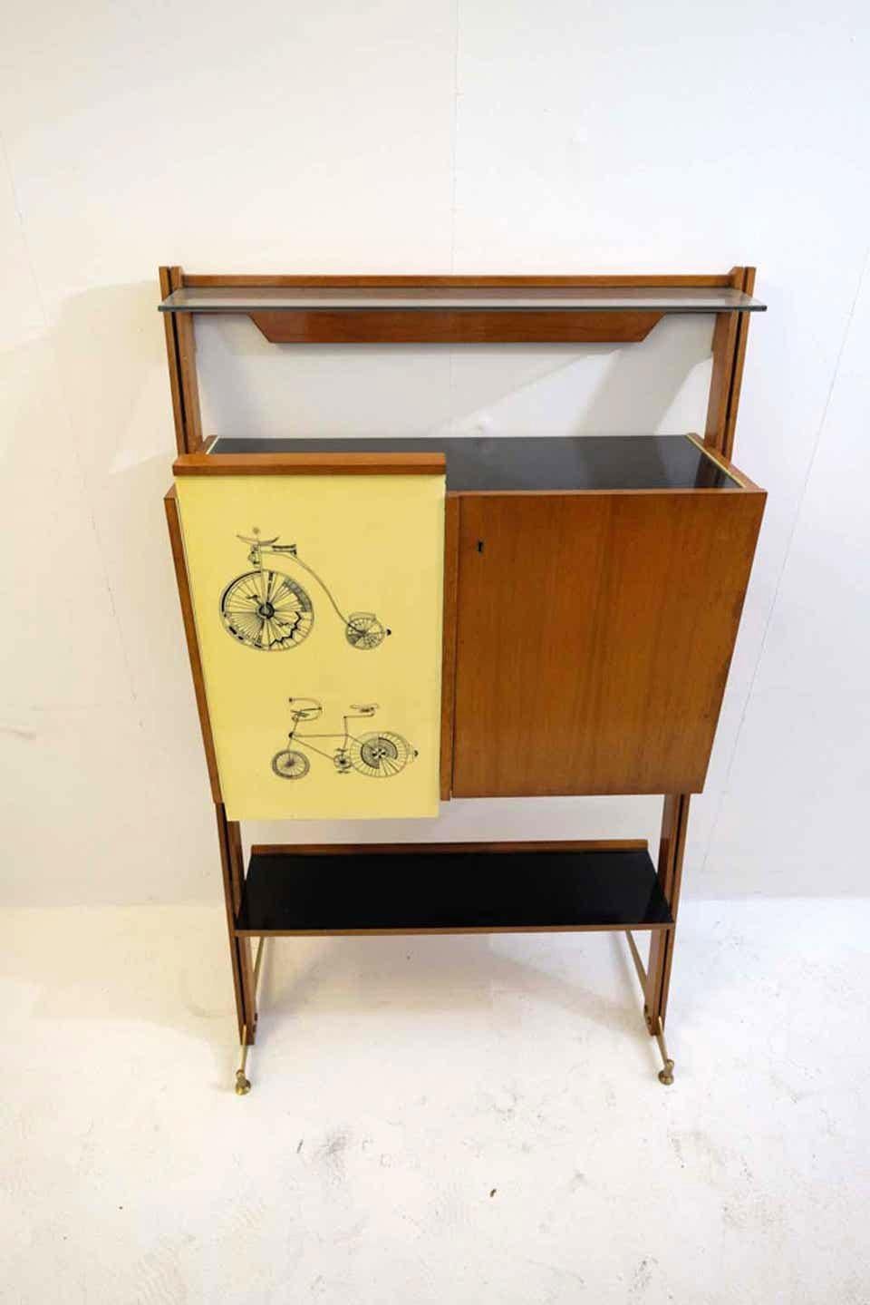 Midcentury Italian bar with original bicycle printed yellow Formica panels on the front.
The body of the cabinet is made in oakwood, with yellow Formica lining on the interior as well as a black Formica plate on the inside of a foldaway table