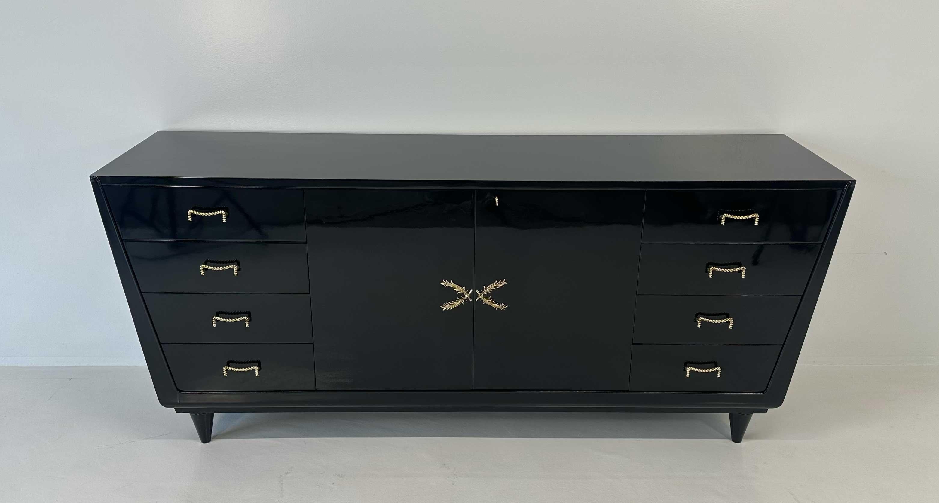 Un'elegante credenza italiana degli anni '50, realizzata in legno laccato nero con raffinati dettagli in ottone, che esemplifica l'influenza dello stile Art Déco sul design italiano del dopoguerra. Le linee pulite e le proporzioni equilibrate sono