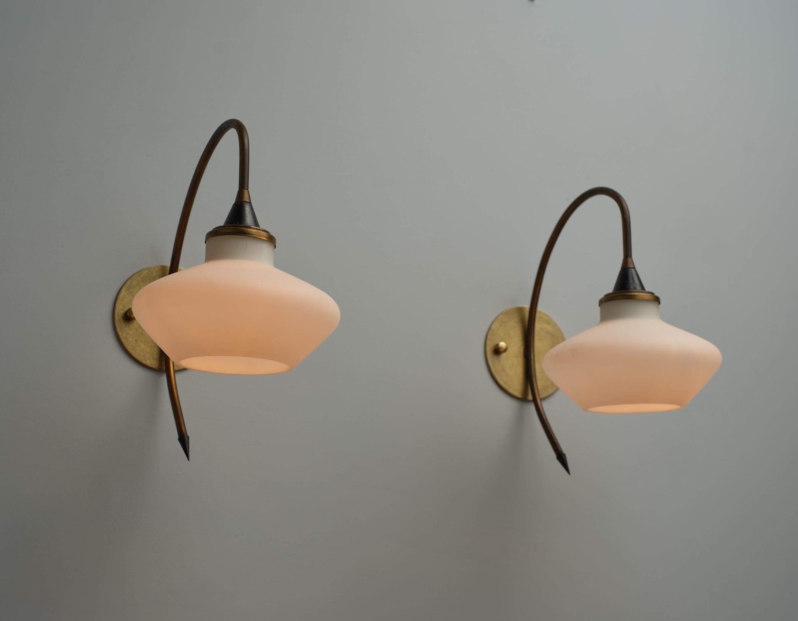 This pair of wall sconces originates from 1950s Italy, showcasing a design characteristic of the period. Each sconce features a shade made from opaline glass, also known as milk glass, which provides a soft, diffuse light suitable for creating a