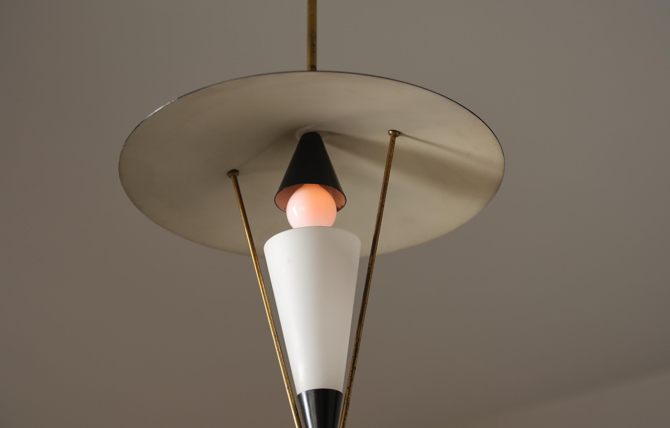 Ceiling-mounted pendant composed of a slender brass down-rod, a black enamel steel canopy, and a shallow circular metal reflector. Three brass struts form an open triangular frame that supports an opaline glass cone diffuser. The bulb sits directly