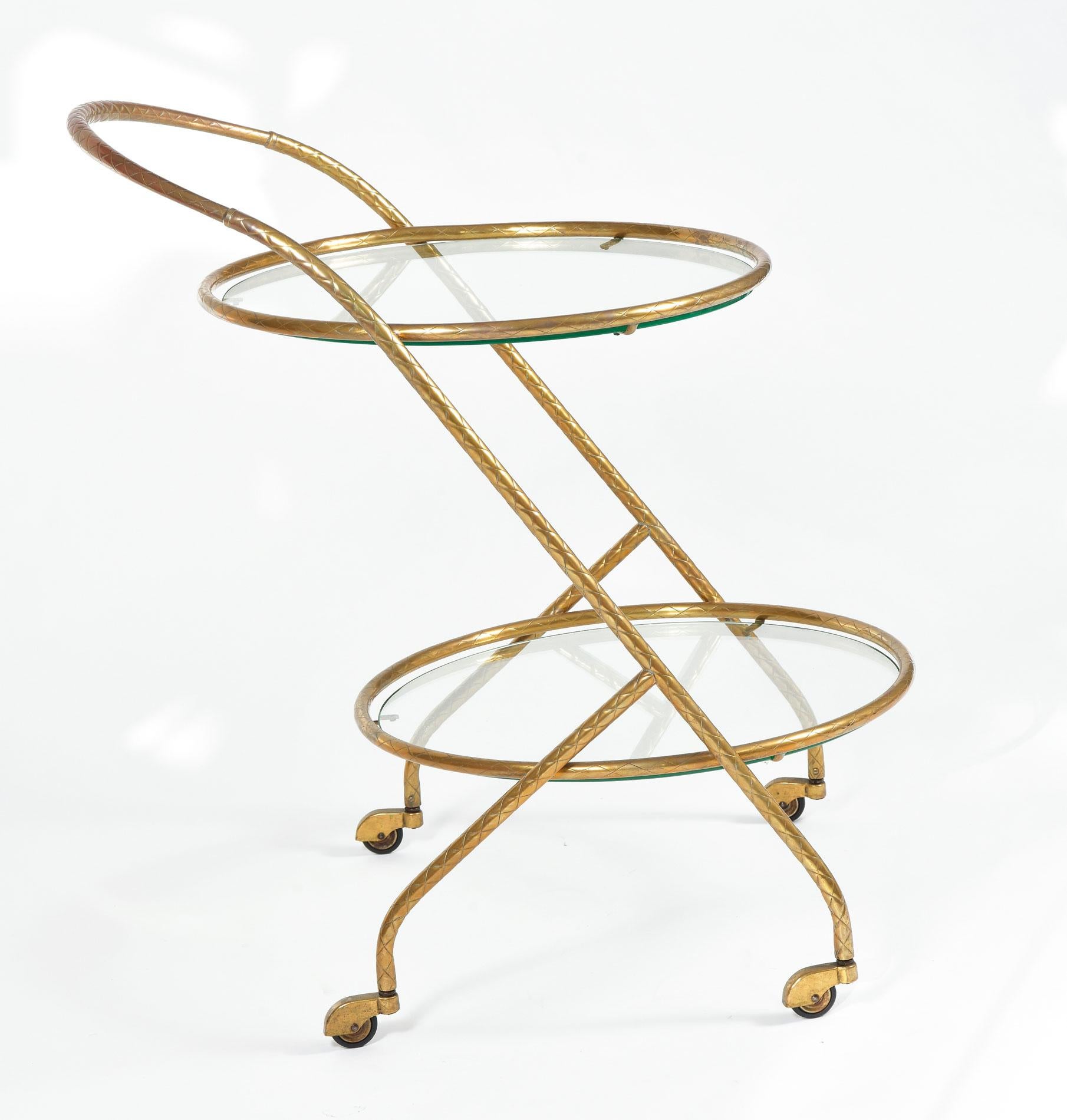 Two-tiered circular drinks trolley. Brass handle, frame and legs are etched with decorative criss-cross patterning. Four matching brass covered caster wheels allow for easy movement.