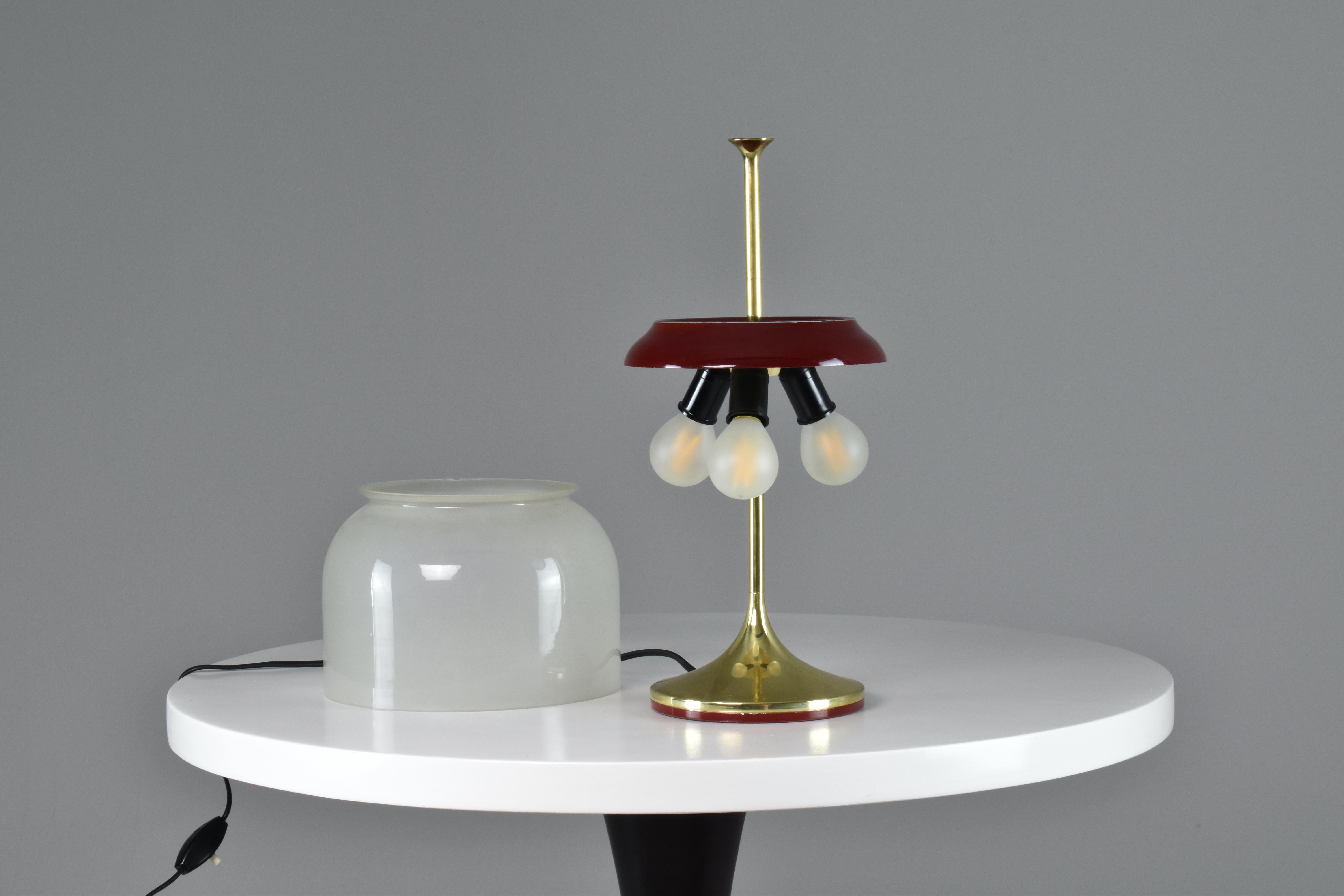 A gorgeous mid-century vintage Italian table lamp designed with a slender brass structure, a removable mushroom-shaped gradient opaque glass shade, and dark red metal details. 
Italy. Circa 1950's. 


 