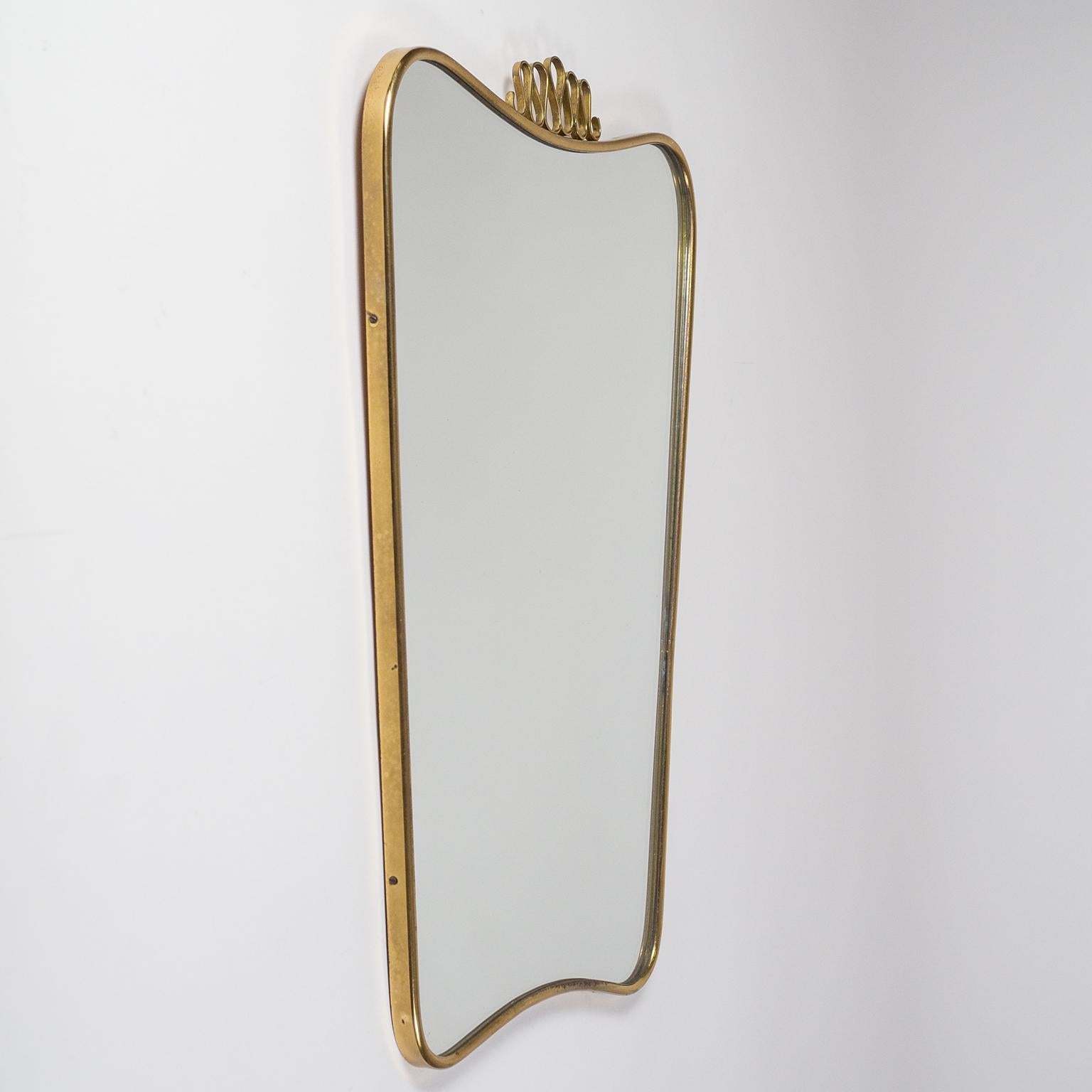 Lovely Italian brass mirror in the style of Gio Ponti. Continuous curved brass rim with an ondulating brass finial. Stamped 