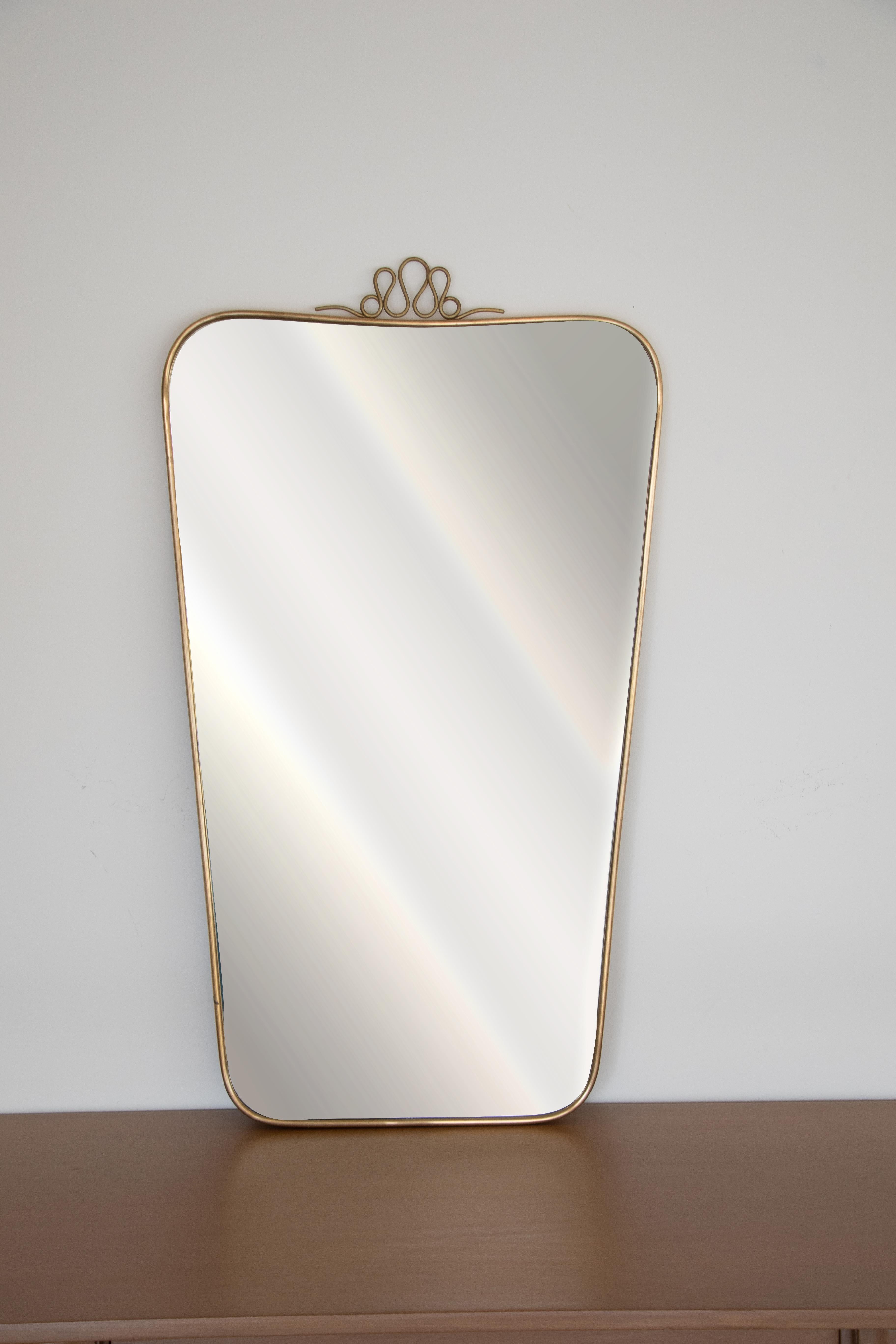 Vintage Italian brass mirror from the 1950s in the style of Gio Ponti. Wood backing with brass frame around wavy mirror and beautiful curly loop top detail. Nice age and patina to brass. 

Additional measurements: Top width 18.5